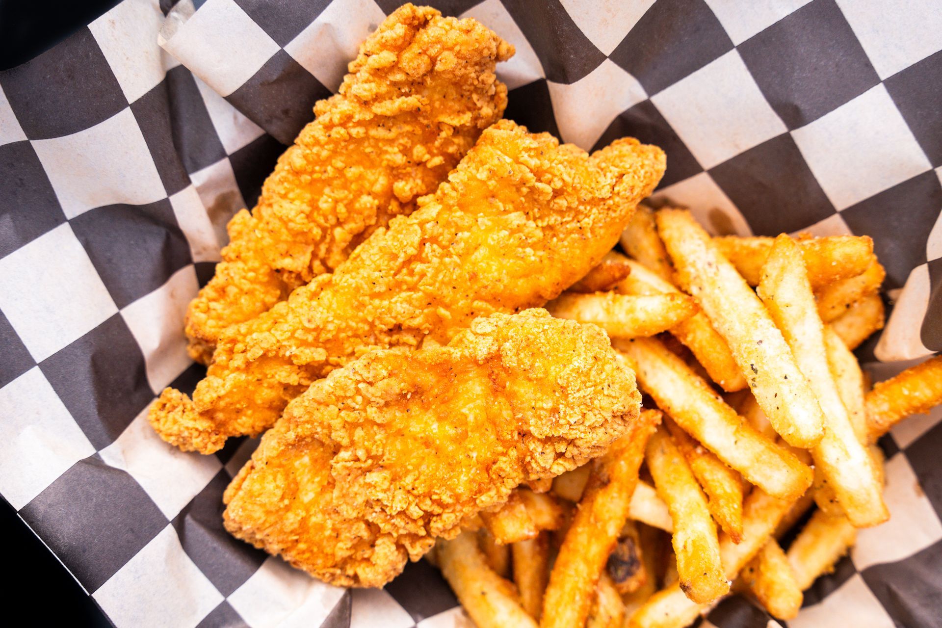 Fried chicken tenders and French fries in a basket lined with black-and-white checkered paper