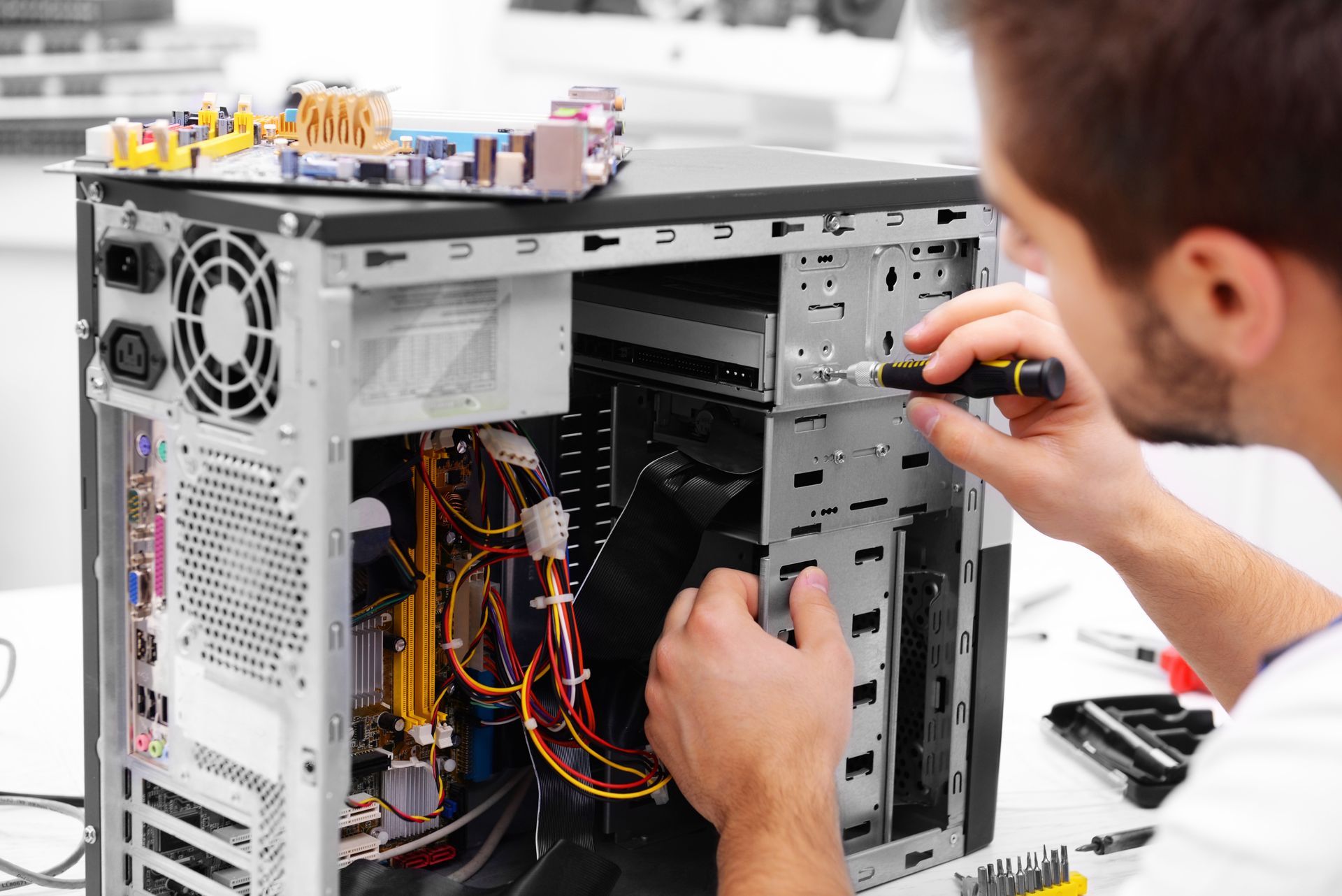 Man repairs computer with screwdriver, PC case open on a white table.