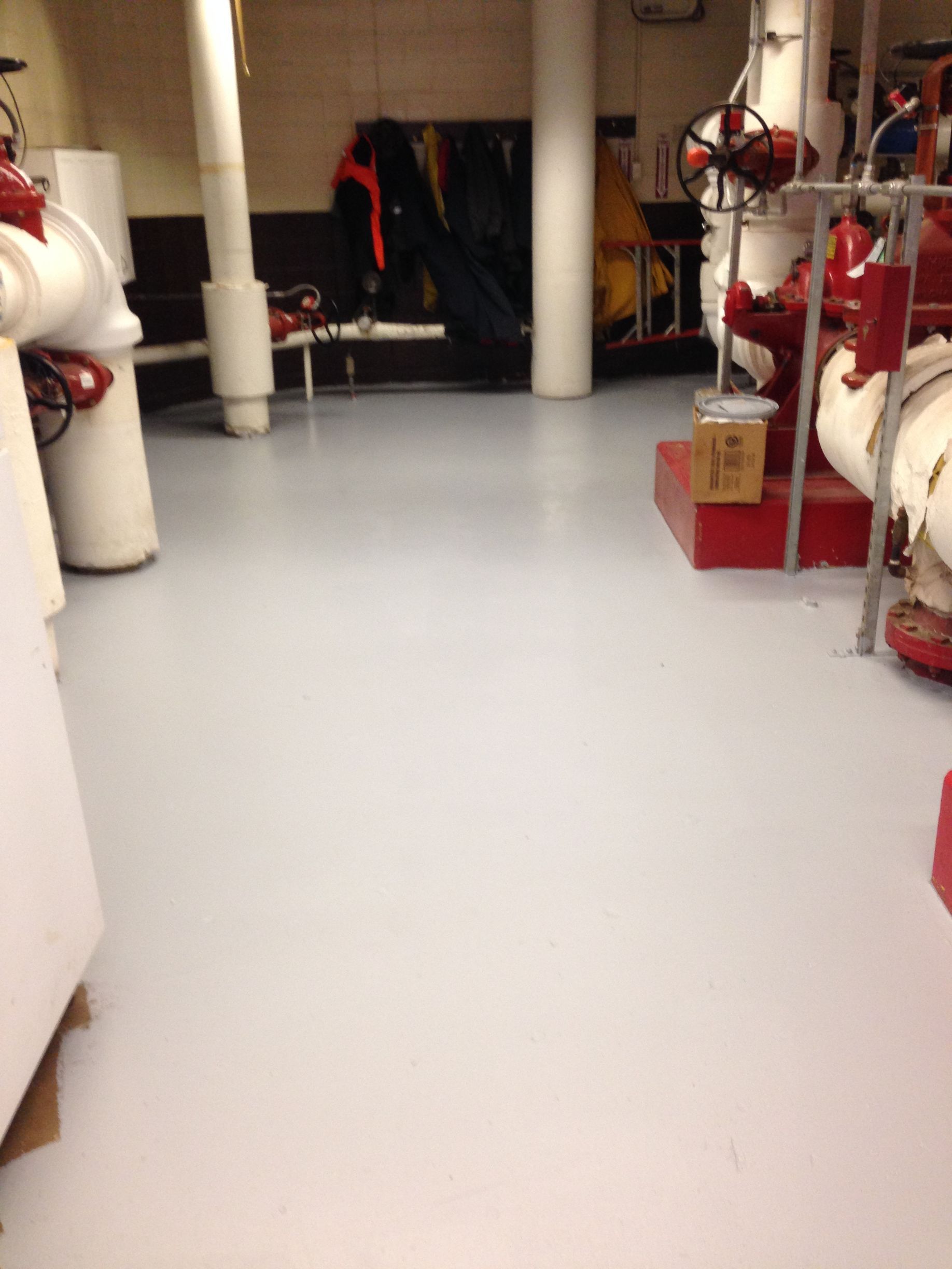 A light gray floor in a utility room, red pipes and valves, white columns, and coats hanging.