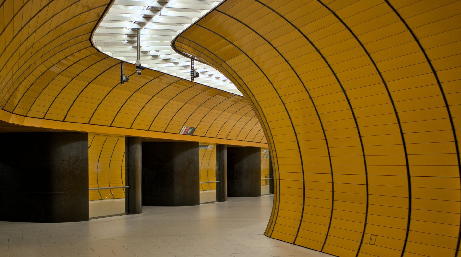 A curved, yellow-paneled subway station hall with dark doorways and a bright, white ceiling.