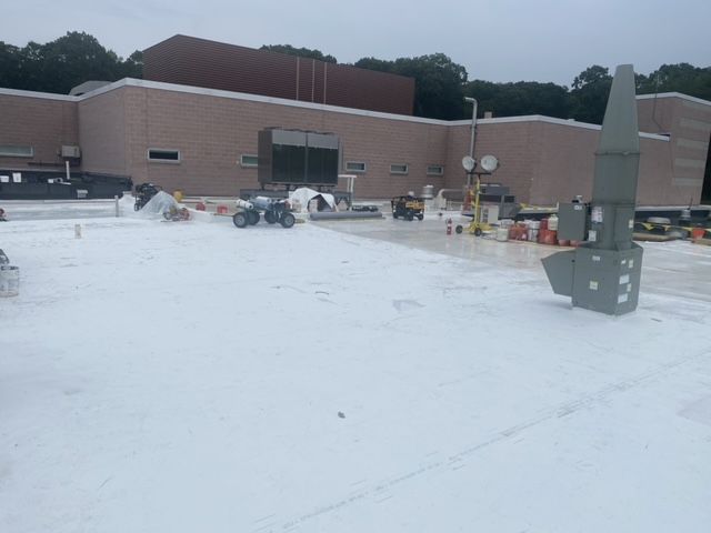 A large building with a white roof is being painted.