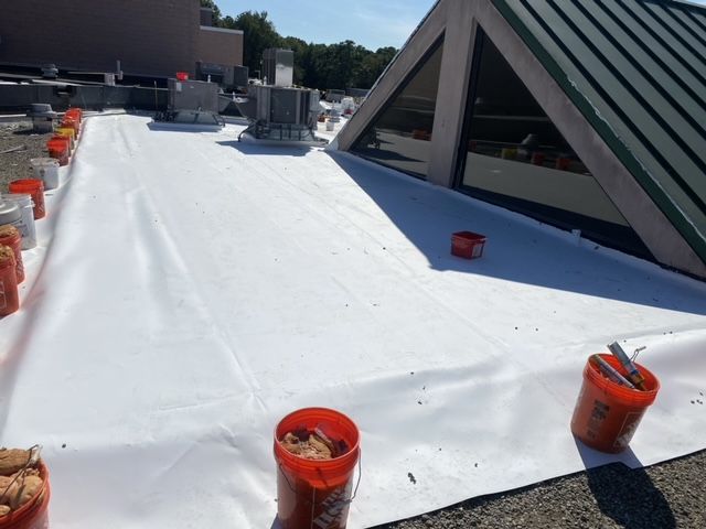 Buckets of dirt are sitting on a white tarp on top of a roof.