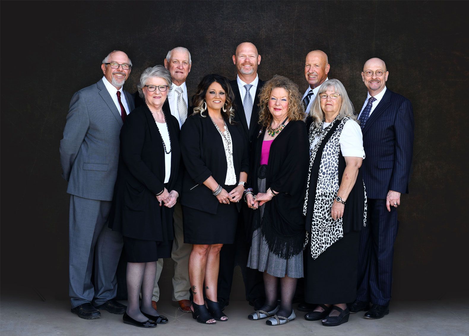 Eight formally dressed people posing together against a dark studio backdrop.