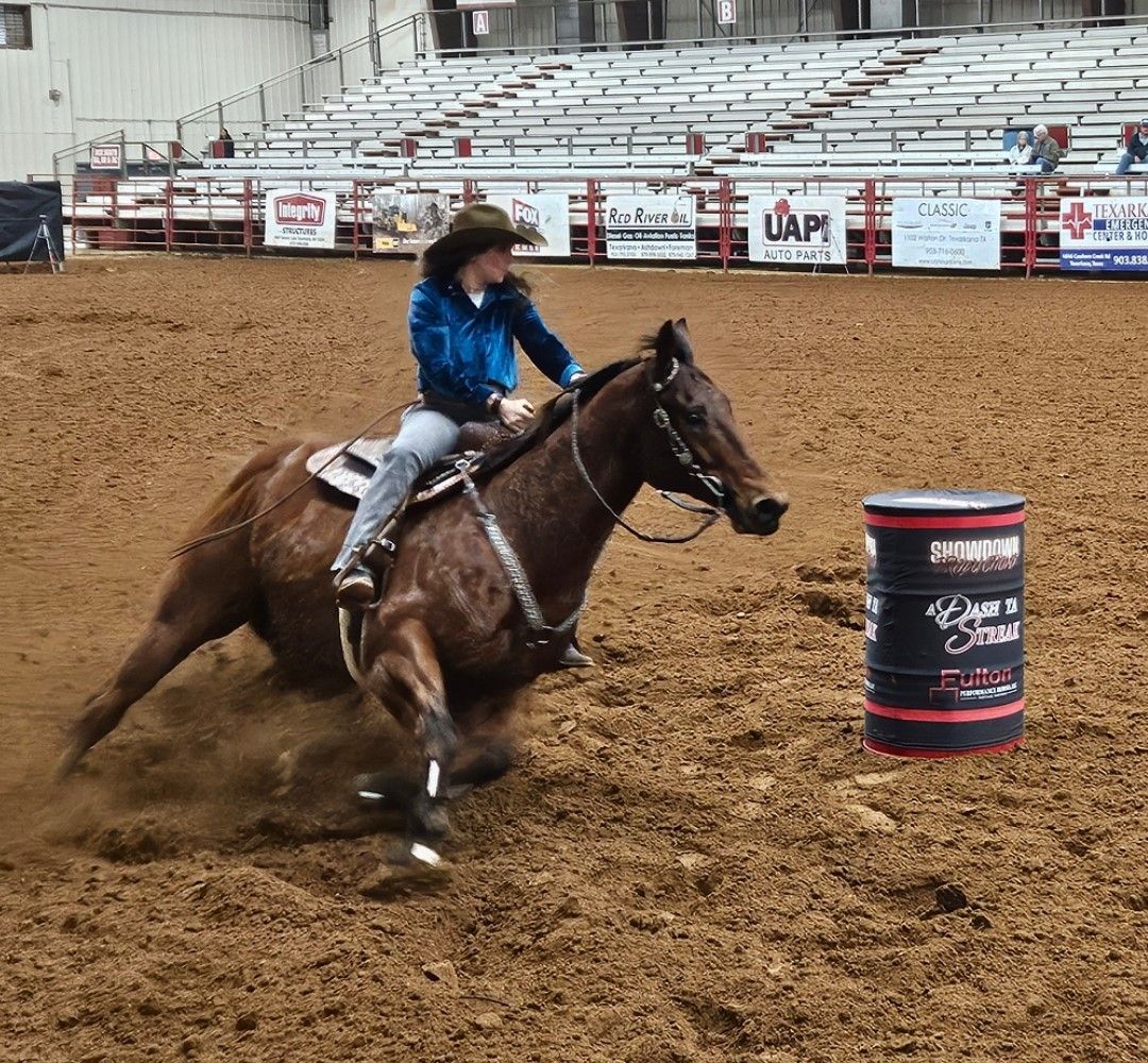 Cowgirl on a brown horse racing around a barrel in an indoor arena