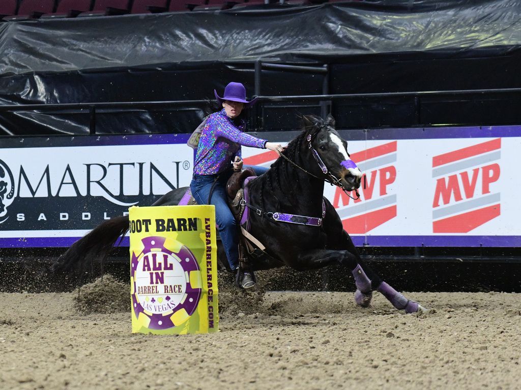 Horse and rider in purple racing around a barrel at an indoor rodeo arena