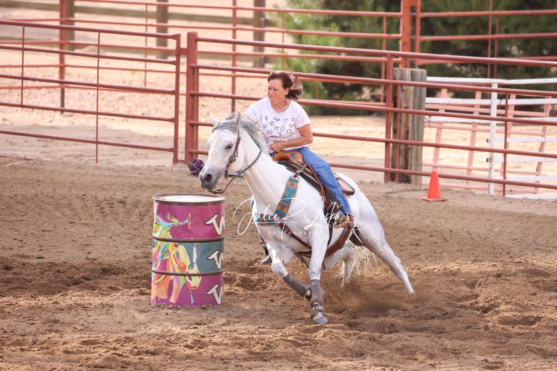 Rider on a white horse rounding a colorful barrel in a dusty rodeo arena