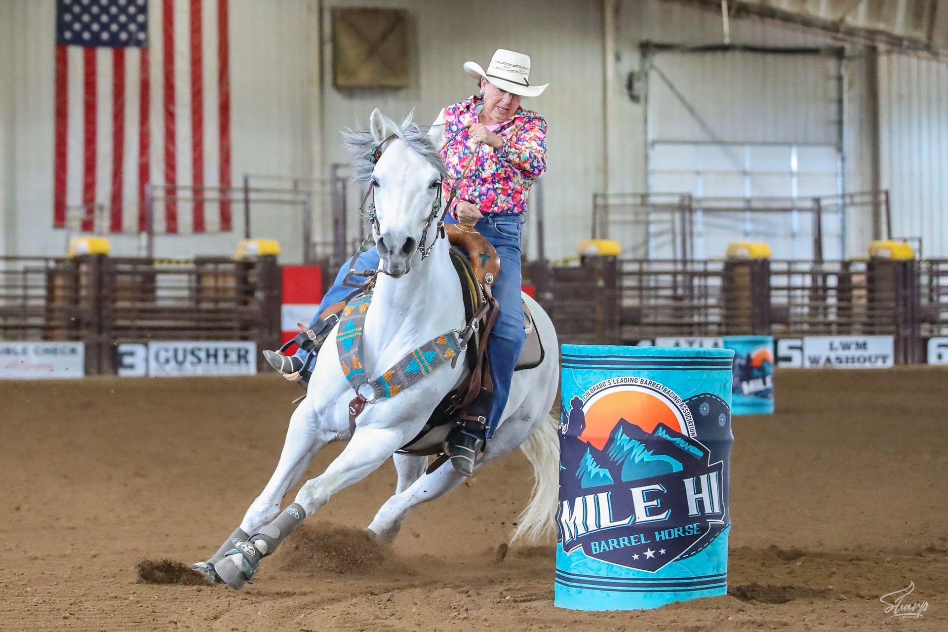 Cowgirl riding a white horse around a barrel in an indoor arena
