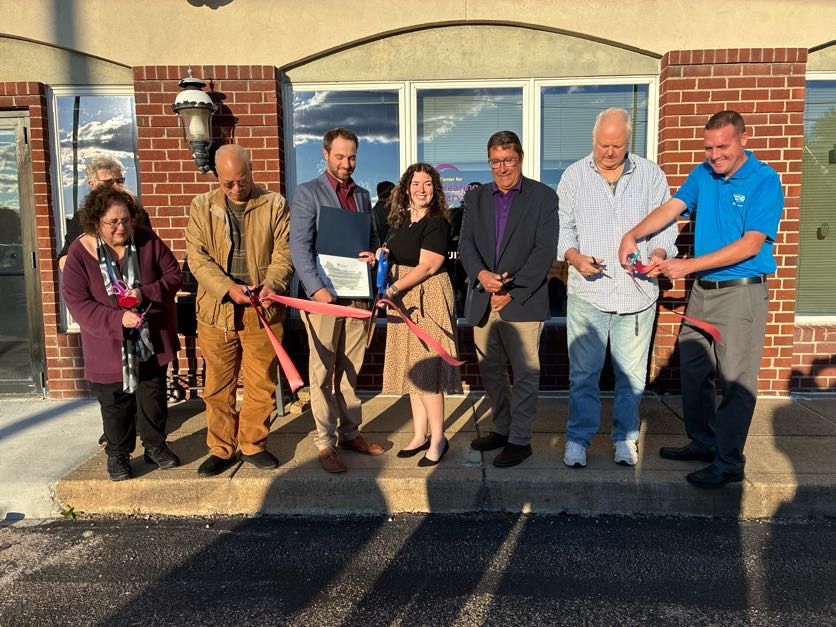 People cutting a ribbon at a brick building opening. Several people smile, holding scissors and ribbon.