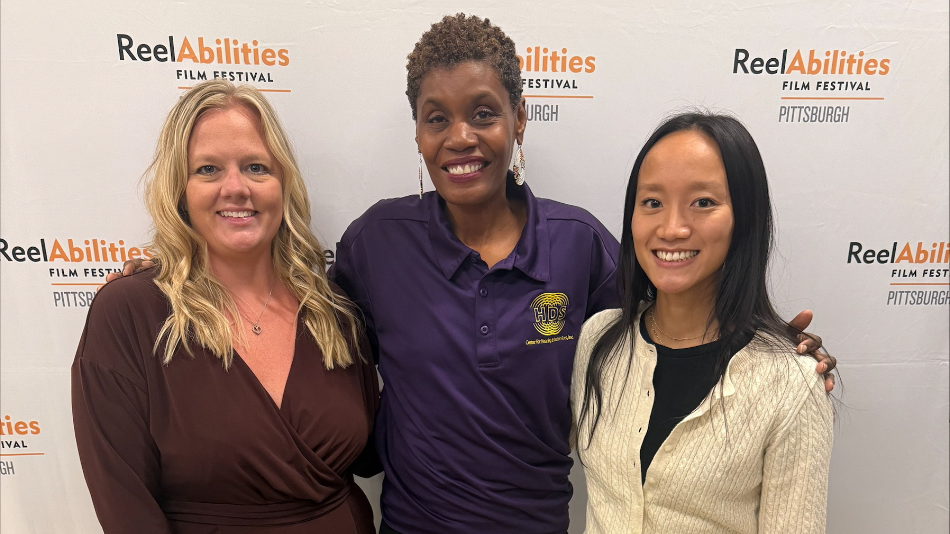 Three people smiling in front of a ReelAbilities Film Festival backdrop.