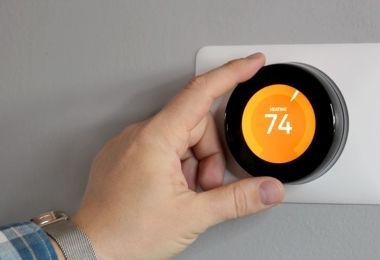 A person is adjusting a thermostat on a wall.
