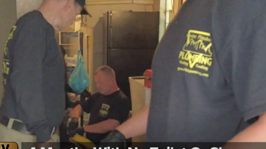 A man wearing a plumbing shirt is standing next to another man