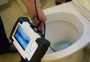 A person is holding a camera over a toilet.