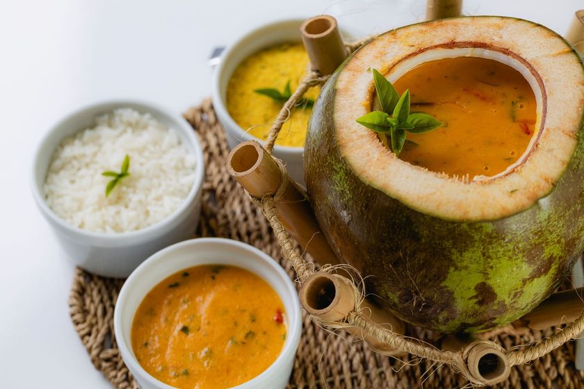 Arroz e caril indianos servidos em panela de barro sobre um jogo americano de palha, acompanhados de arroz e chutneys.