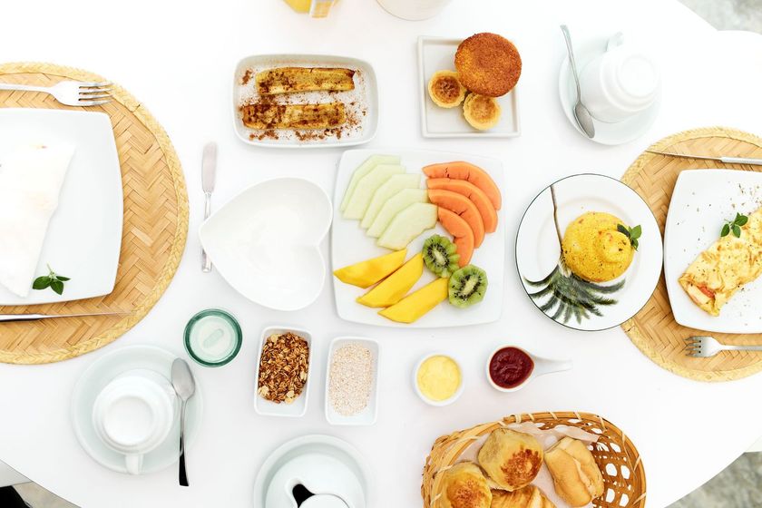 Café da manhã posta de cima para baixo sobre uma mesa branca, com frutas, doces, ovos, café e torradas.