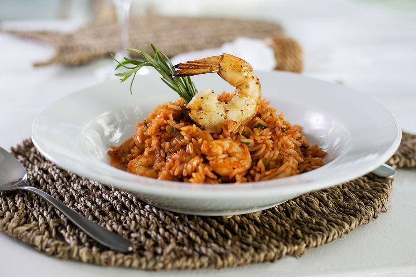 Risoto de camarão em um prato branco com guarnição, sobre um jogo americano de palha com um garfo por perto.