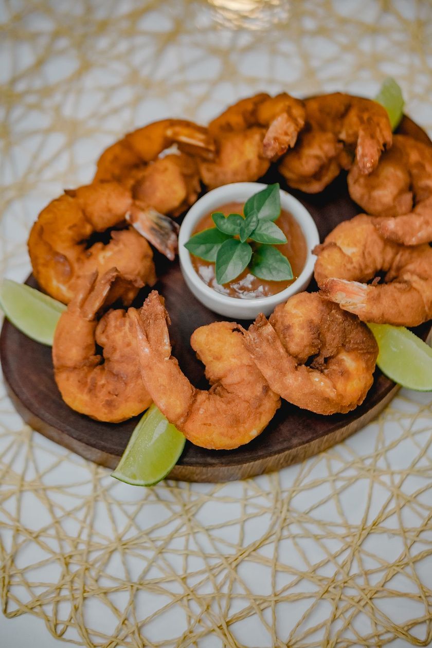 Salgadinhos fritos variados e dourados em um prato escuro, acompanhados de uma tigela pequena com molho.