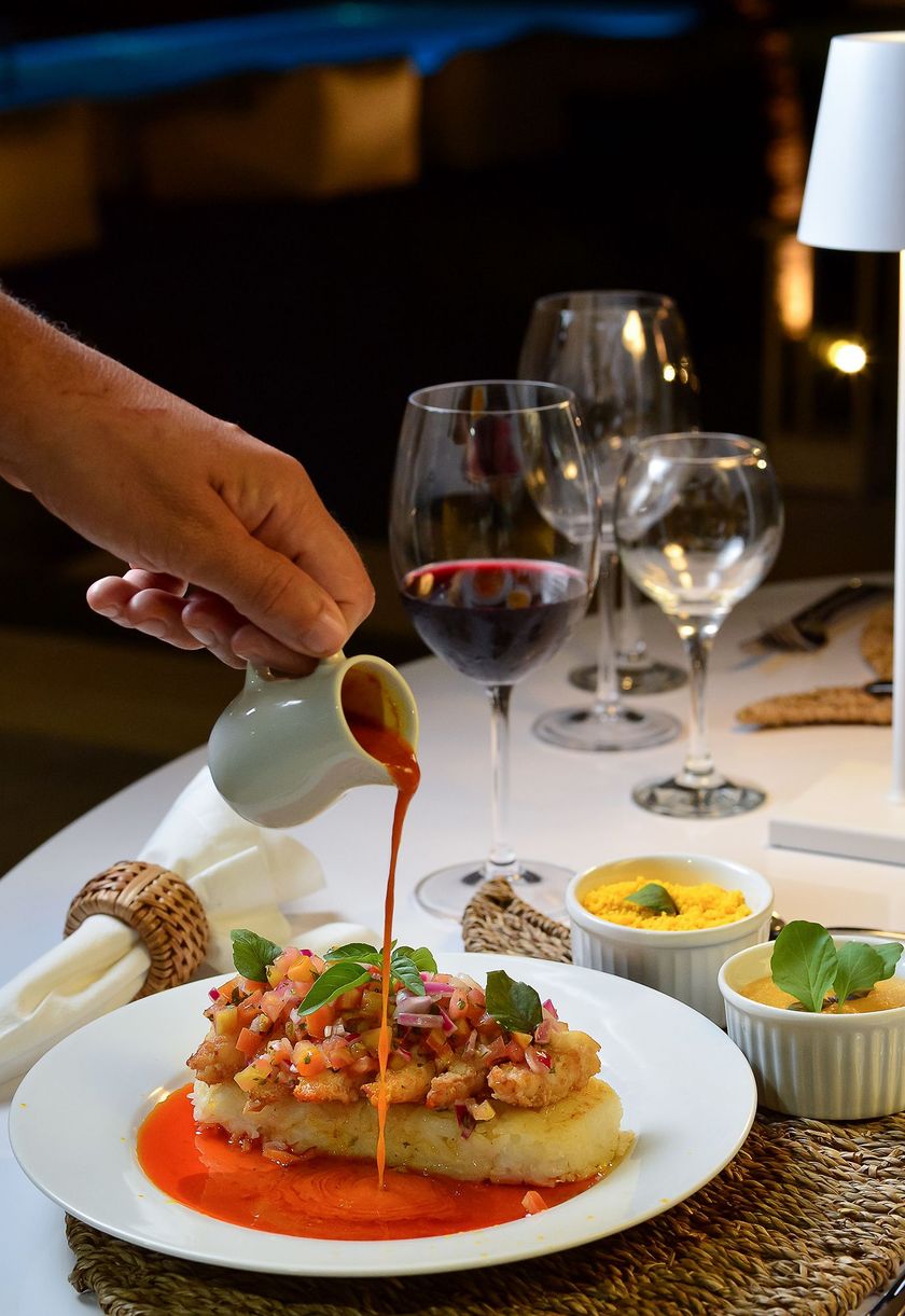 Despeja molho vermelho à mão sobre um prato gourmet em uma mesa de restaurante à luz de velas.