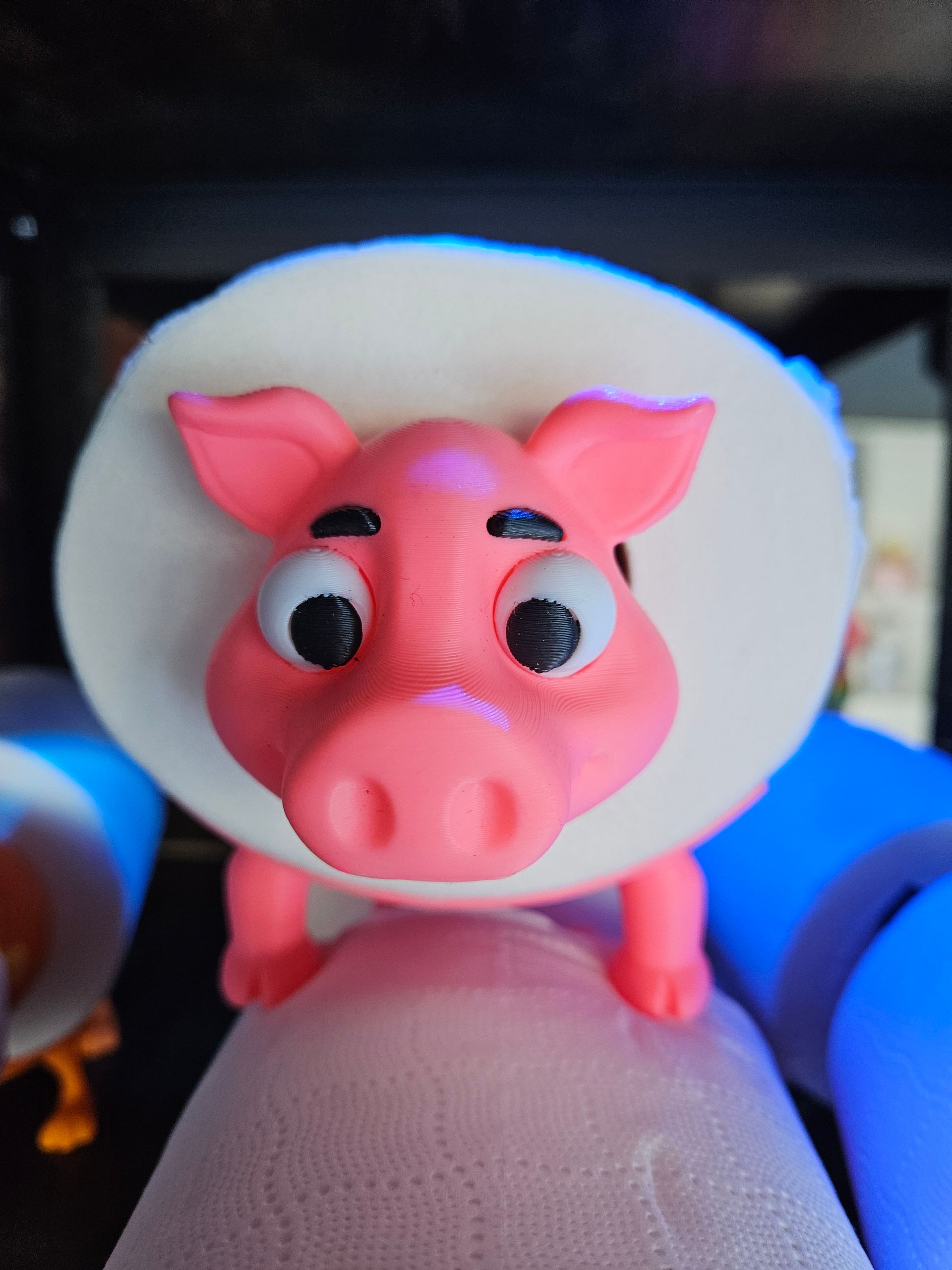 Pink pig figurine with big eyes and a white hat, held between fingers against a dark background