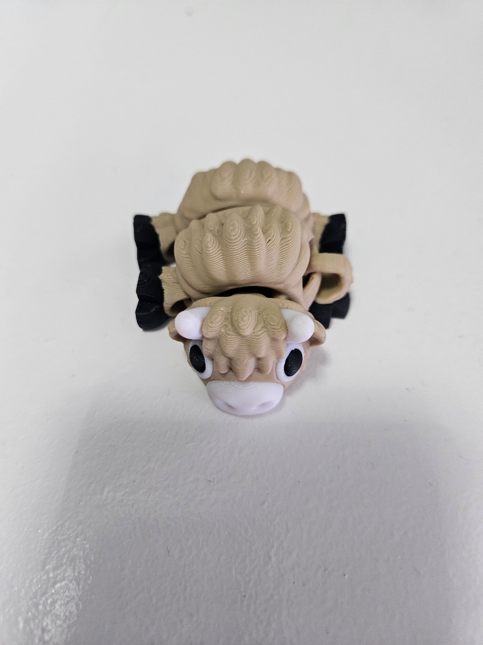 A small, tan sheep figurine with black hooves and ear markings, on a white surface.