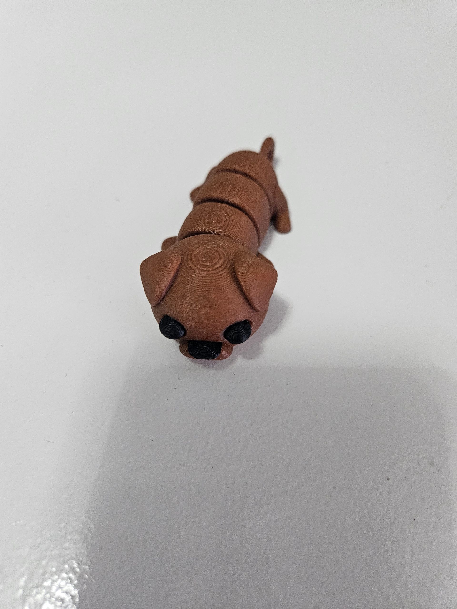 Brown dog figurine on a white surface, facing down.