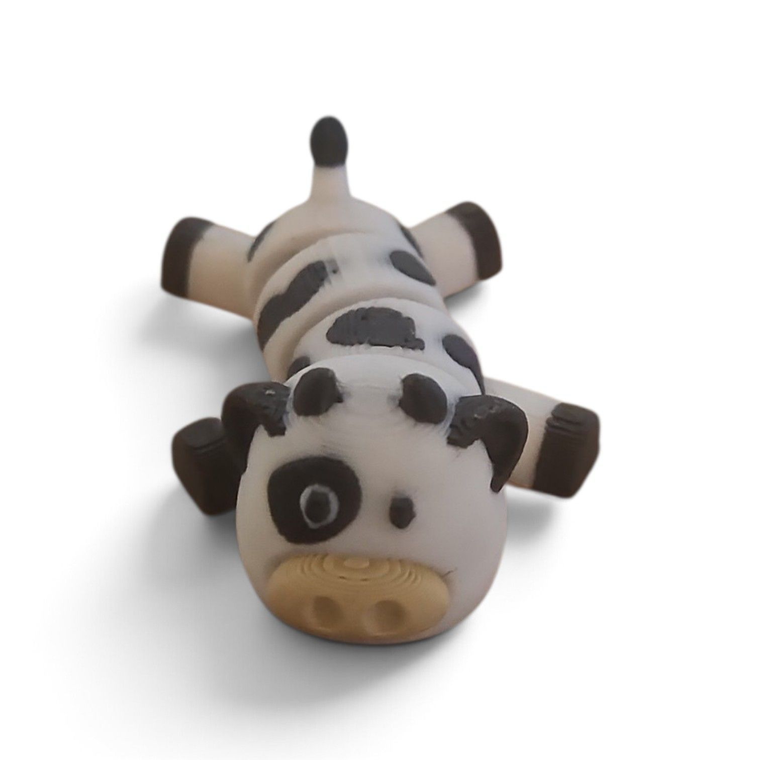 Small black-and-white spotted cow figurine lying on its back on a white background