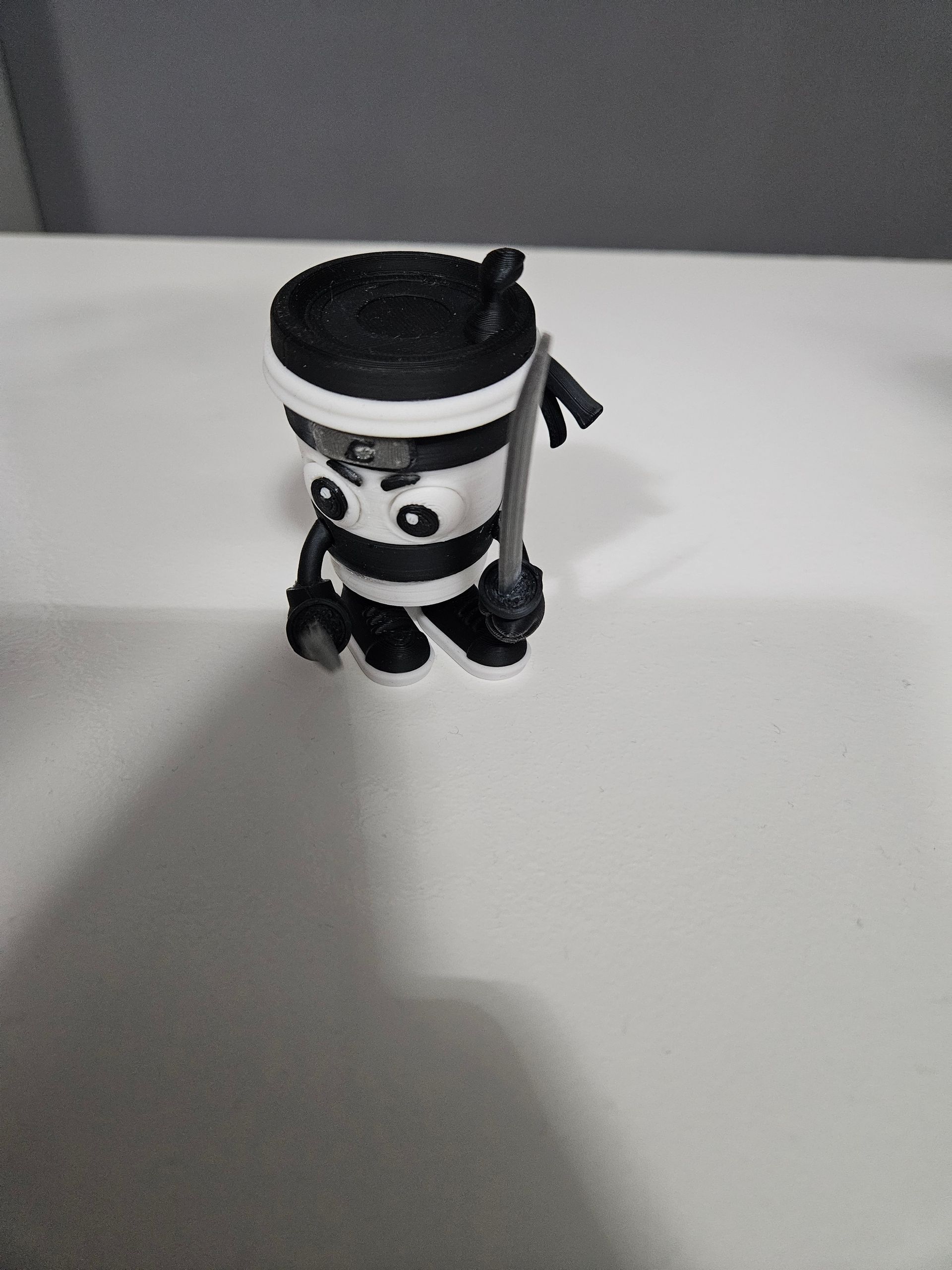 Small black-and-white toy figure with a white hat standing on a white table.