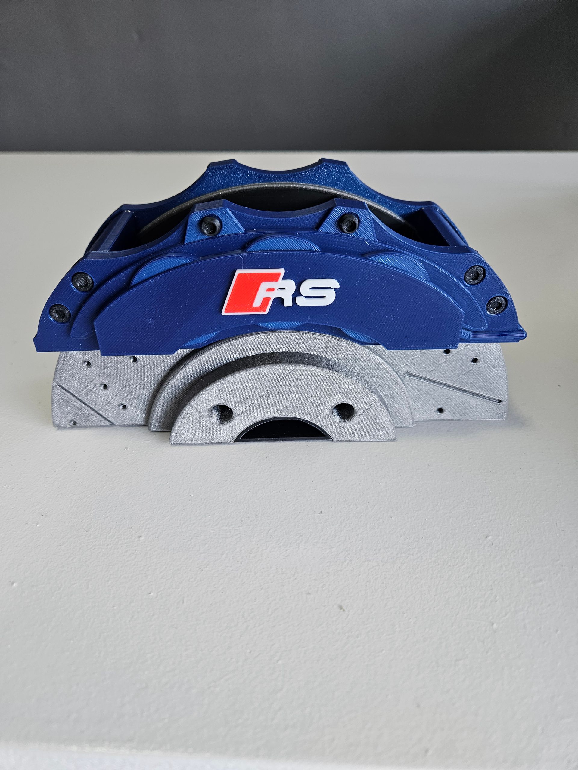3D-printed model of a blue and silver RS brake caliper and rotor on a white surface.