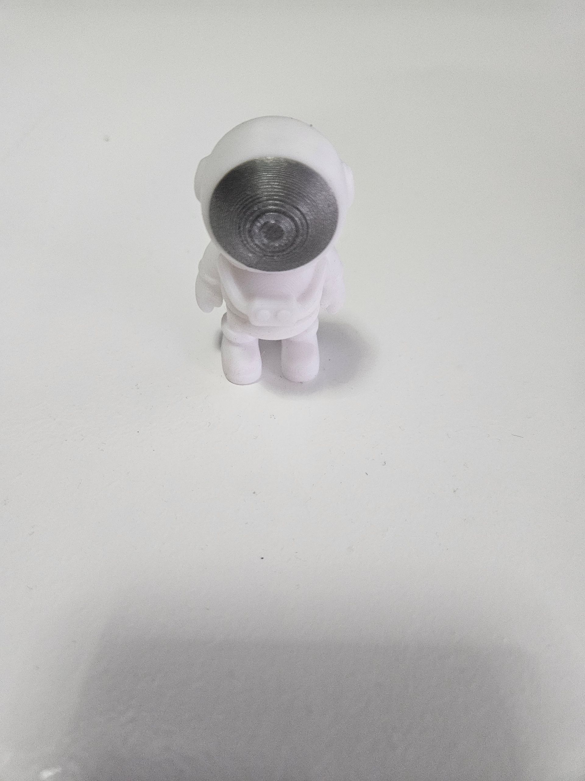 White astronaut toy on a white surface, casting a shadow below.