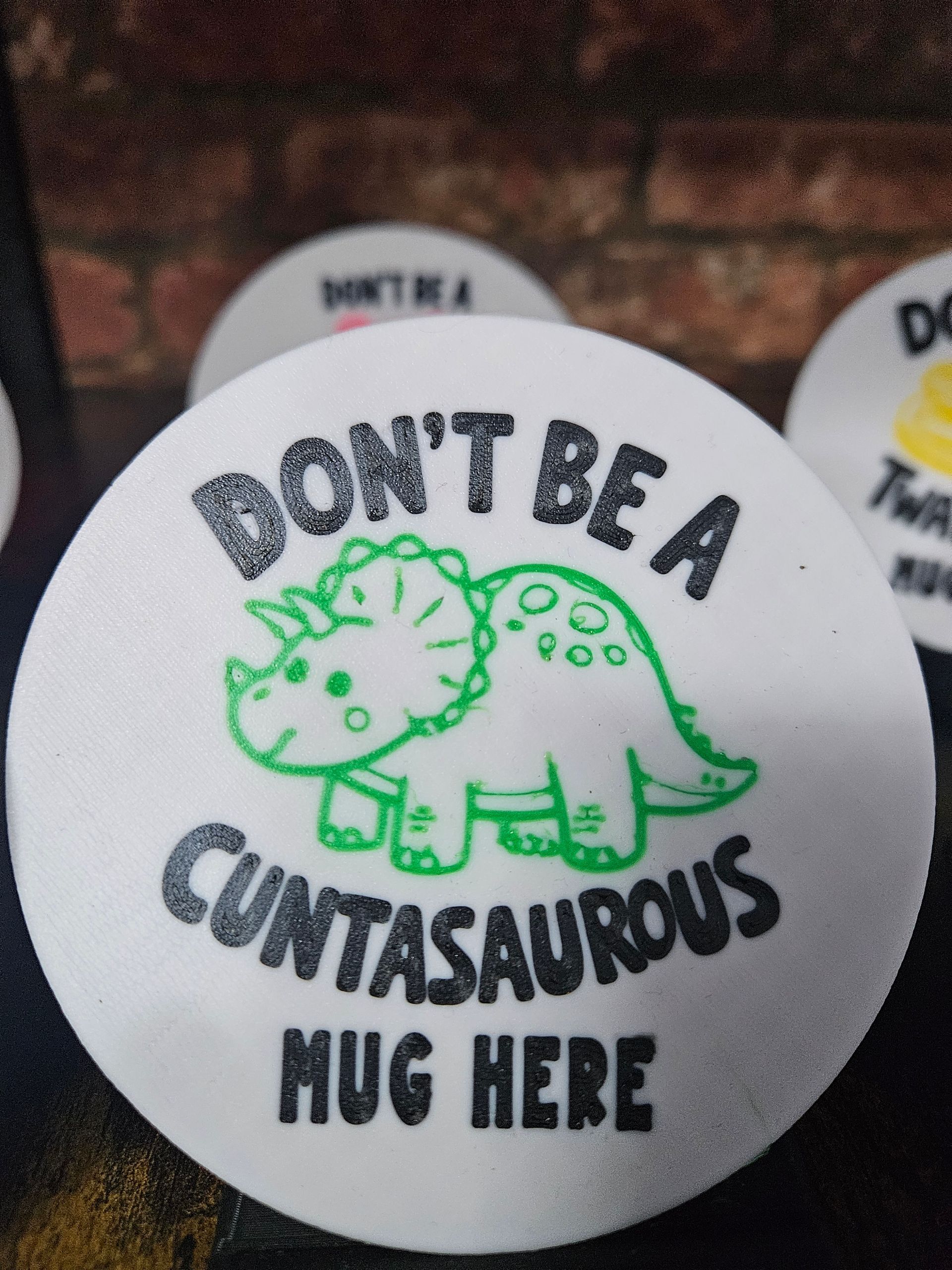 White, circular coaster with a green dinosaur and the text