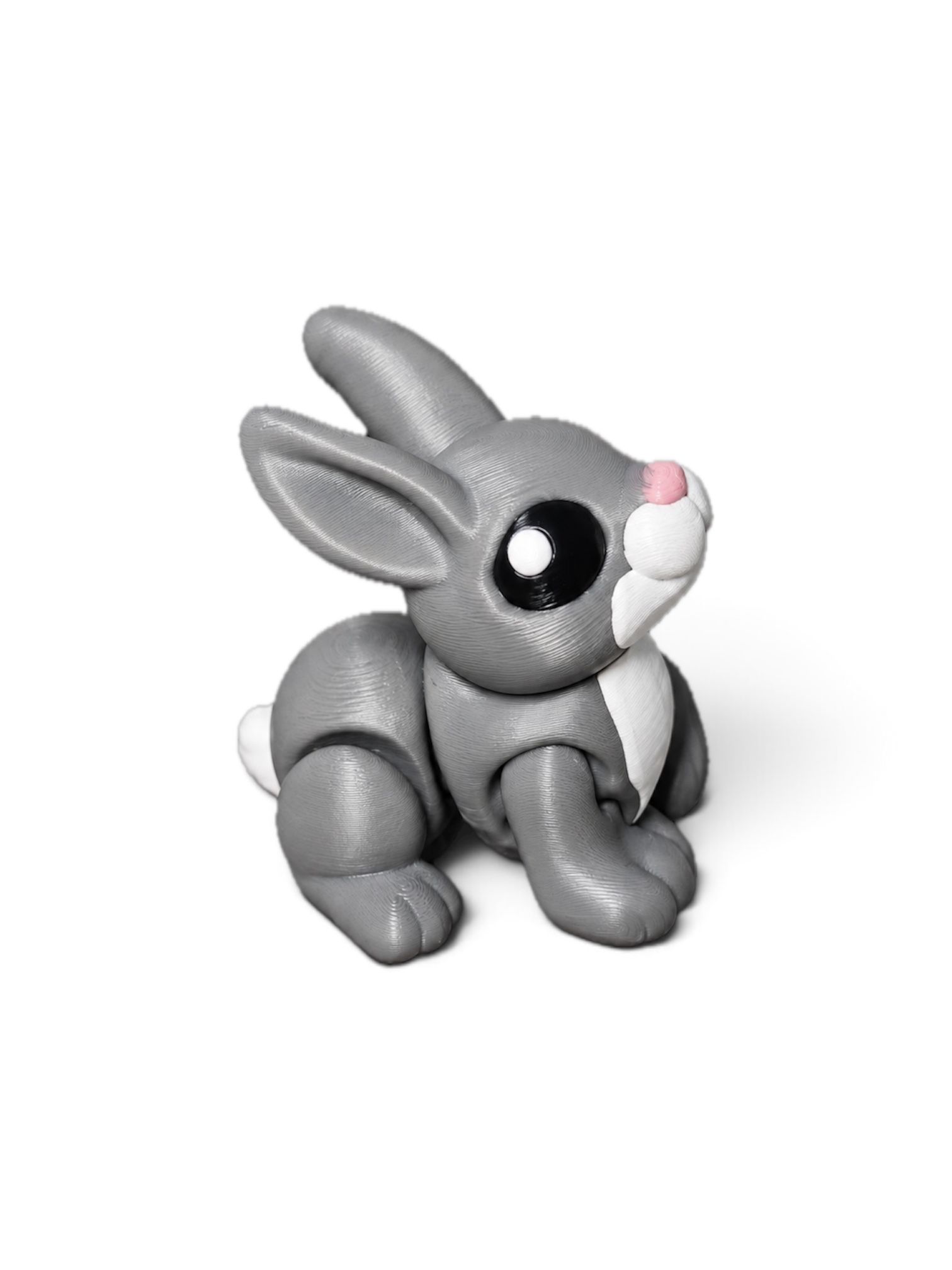 Gray cartoon rabbit figurine with big black eyes and pink nose, sitting on a white background