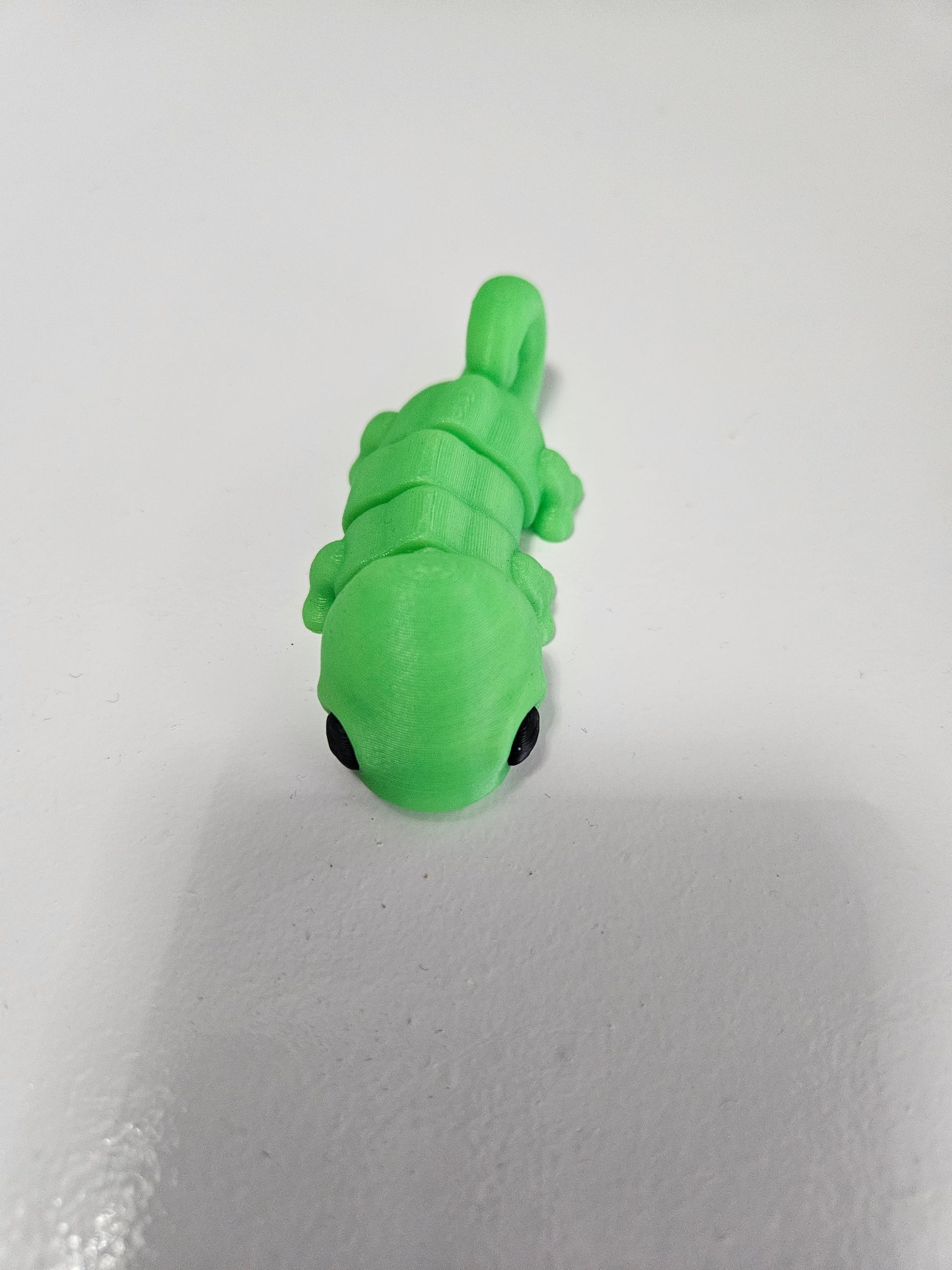Green, fuzzy, lizard-shaped toy with black eyes on white surface.