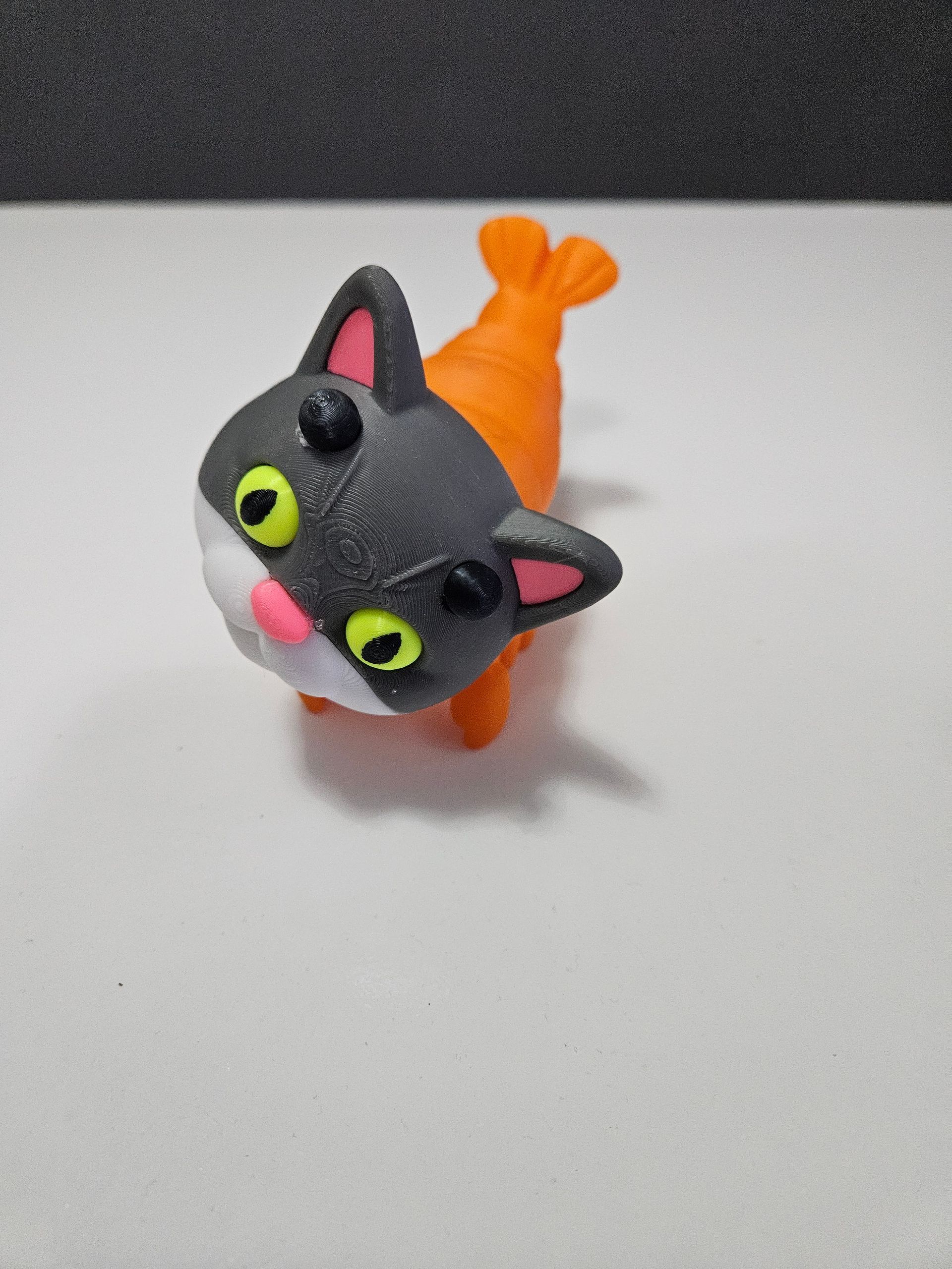 Small black-and-orange cat figurine with bright green eyes on a light surface