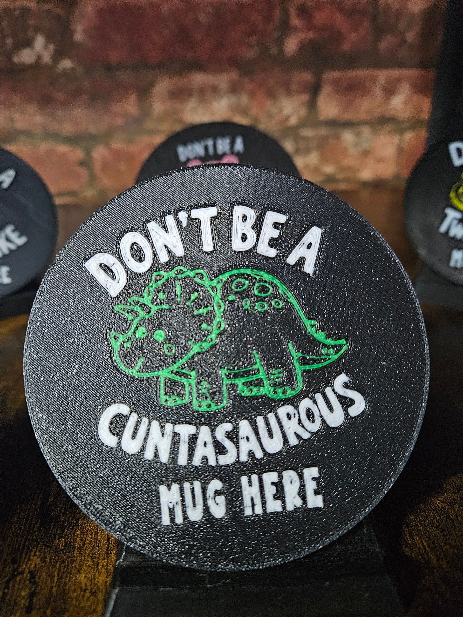 Black coaster with a green dinosaur and the words