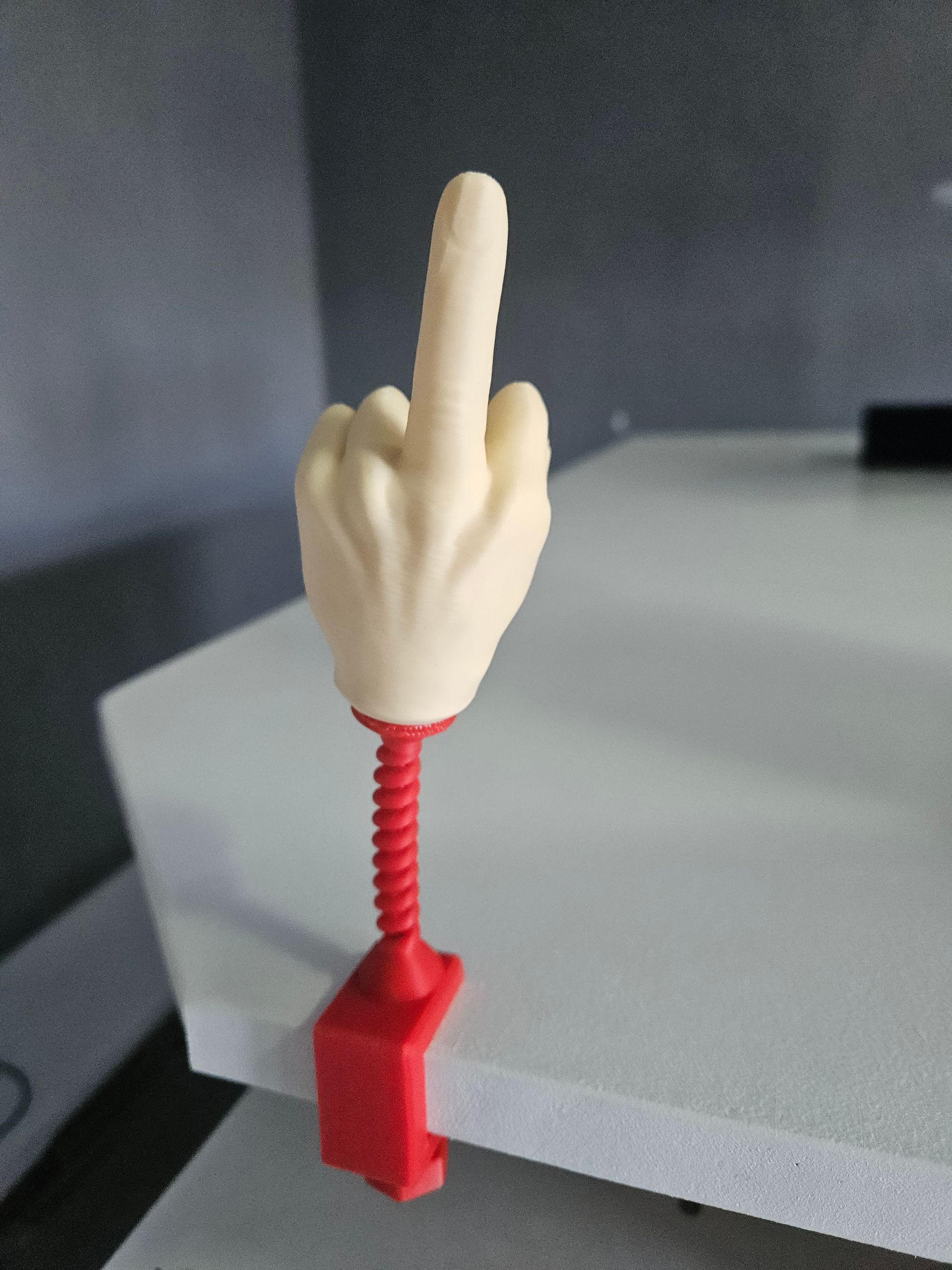 Red clamp with beige hand giving the middle finger, attached to a red spring.
