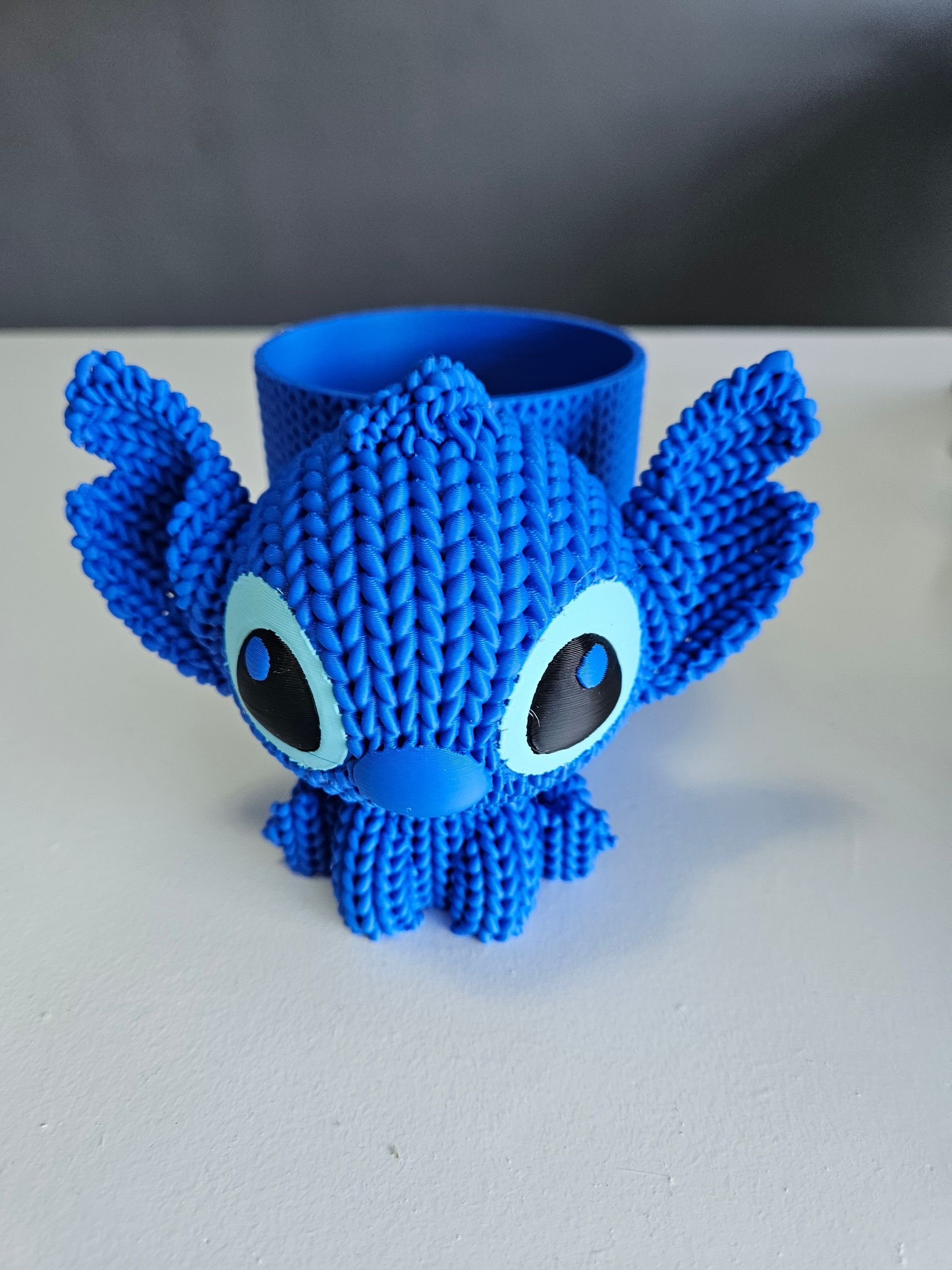 Blue 3D-printed Stitch planter with large ears, black and white eyes, and a cylindrical pot.