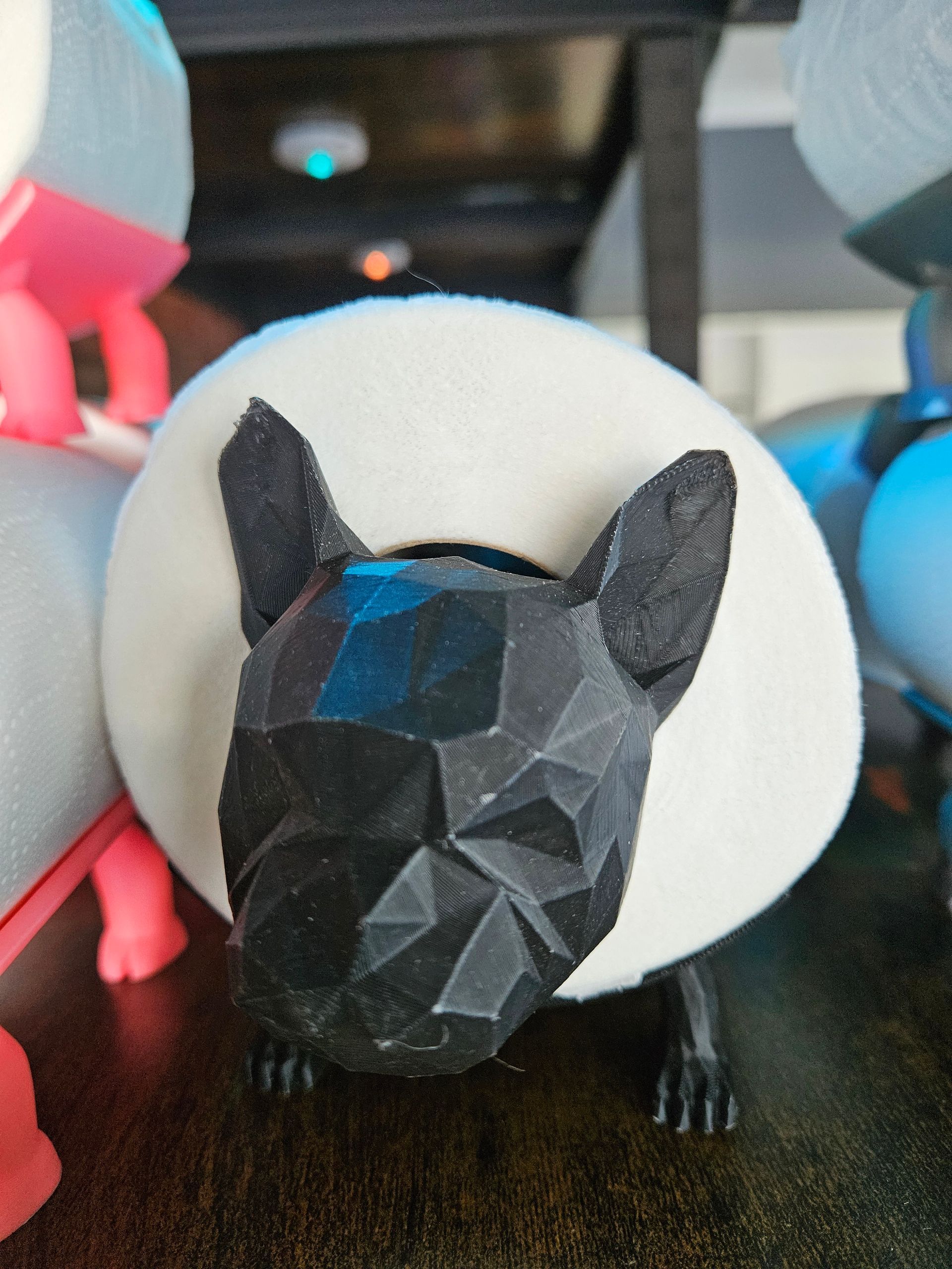 Black faceted dog figurine with a white donut-shaped collar, surrounded by colorful toys.