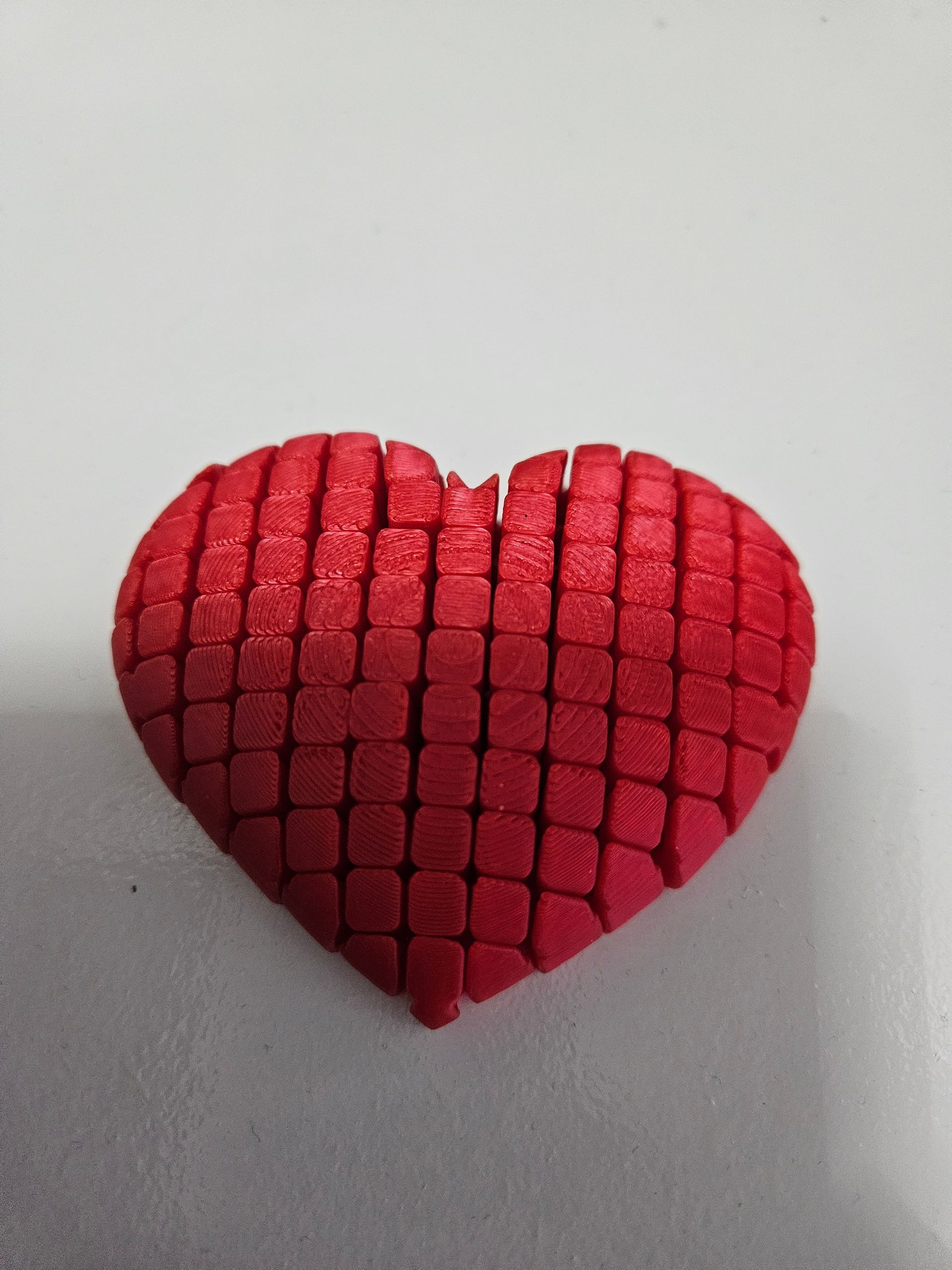Red heart-shaped object made of small square blocks, on a white surface.
