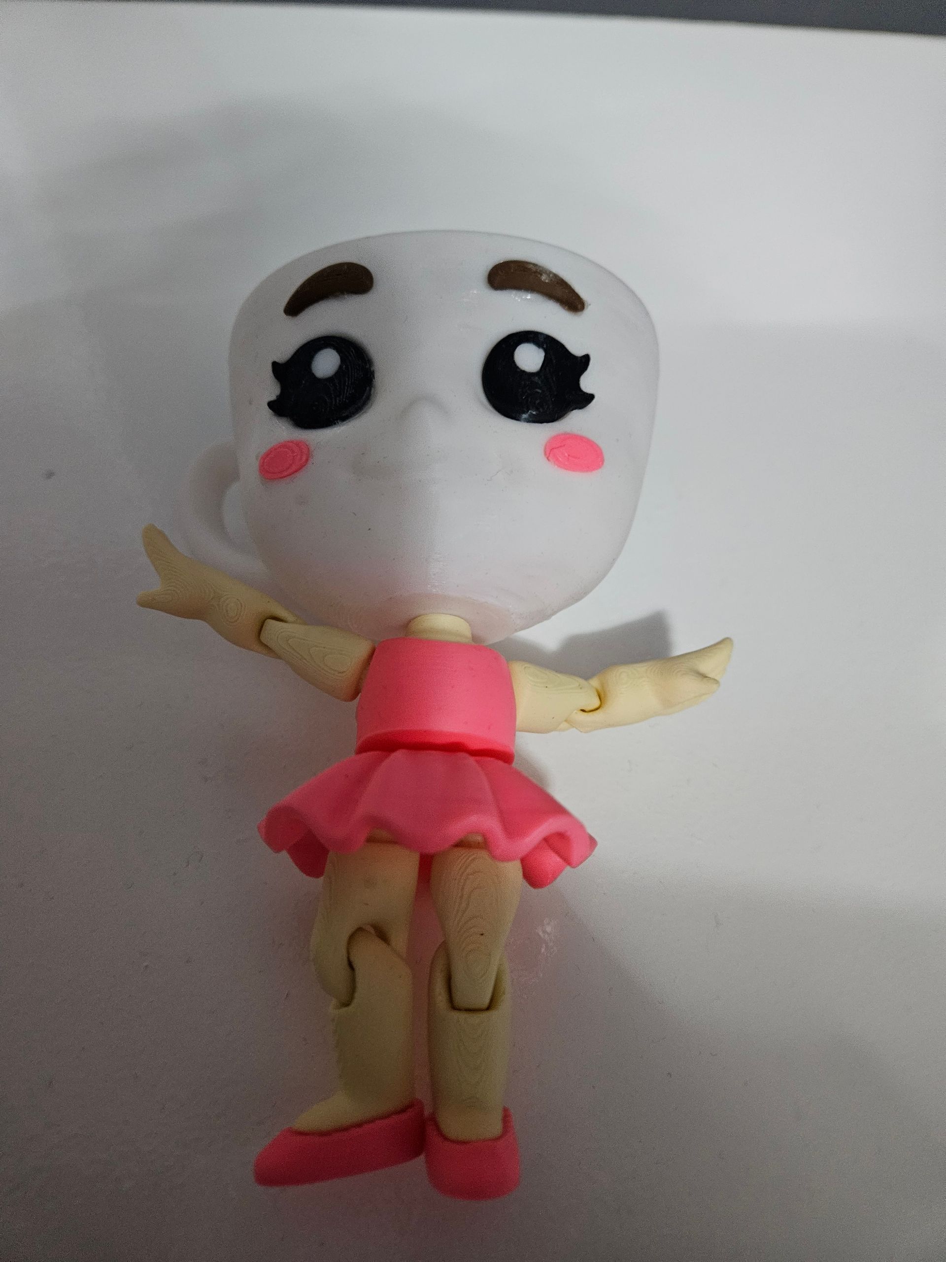 Cute white doll with big black eyes, pink cheeks, pink dress, and outstretched arms on a plain background
