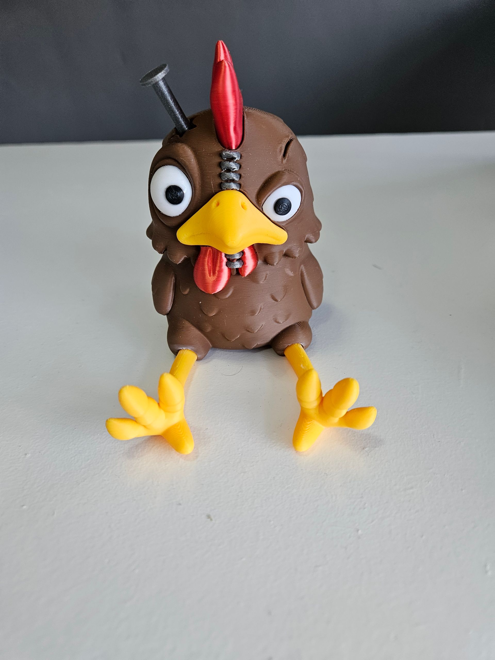 Brown cartoon chicken with a nail in its head, red comb, yellow beak and legs, angry expression.