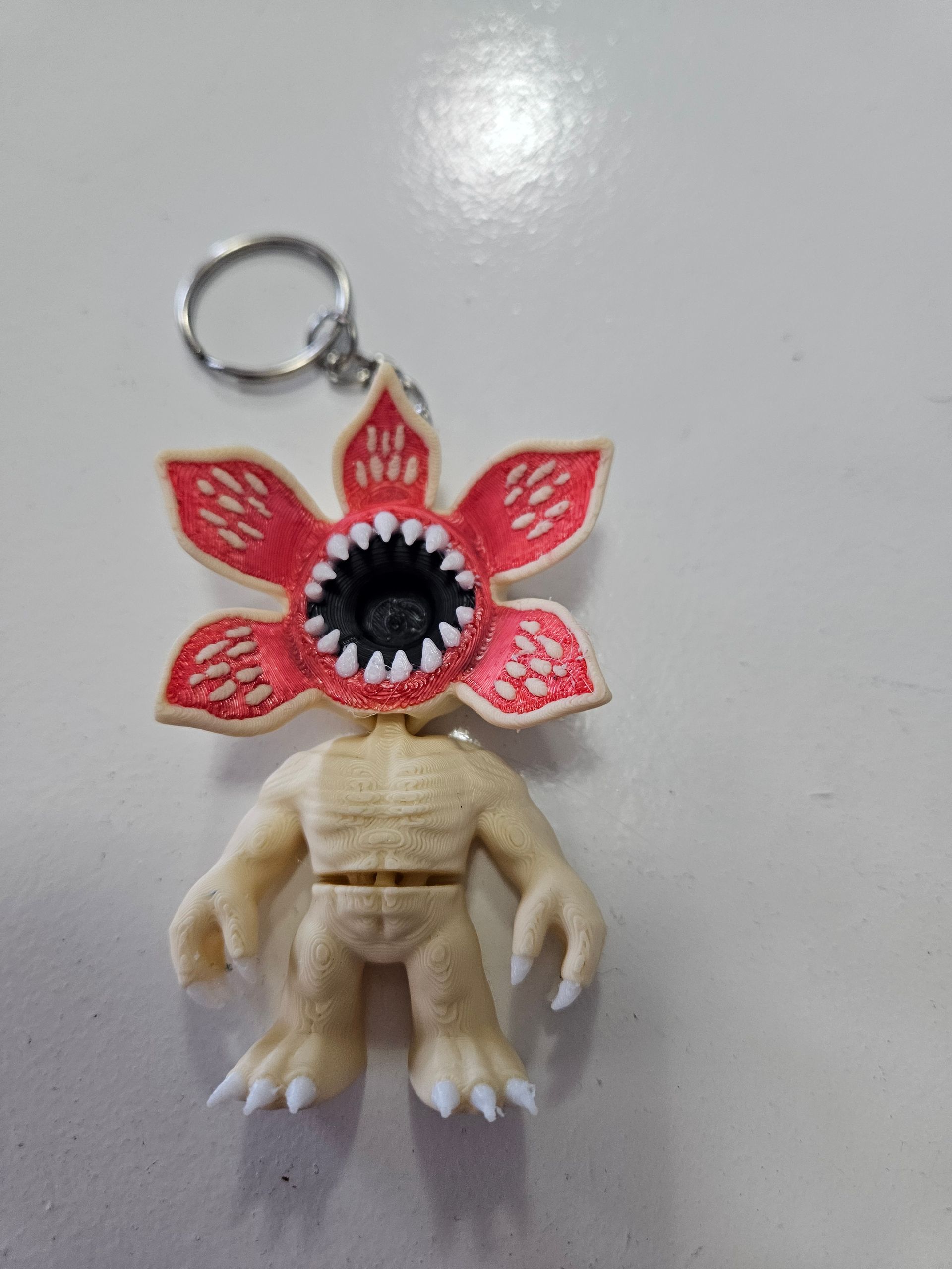 Demogorgon keychain with red petals, white teeth, and beige body, lying on a white surface.