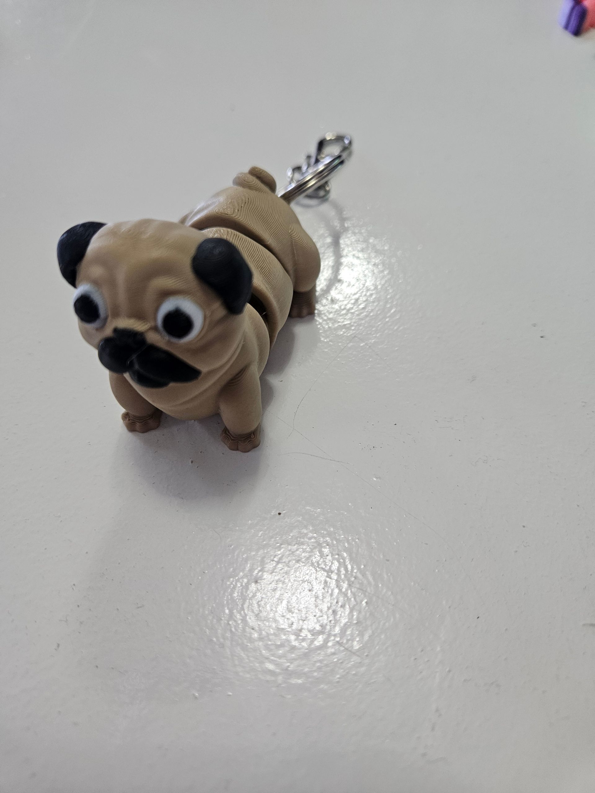 Pug dog keychain, tan and black, on a white surface.