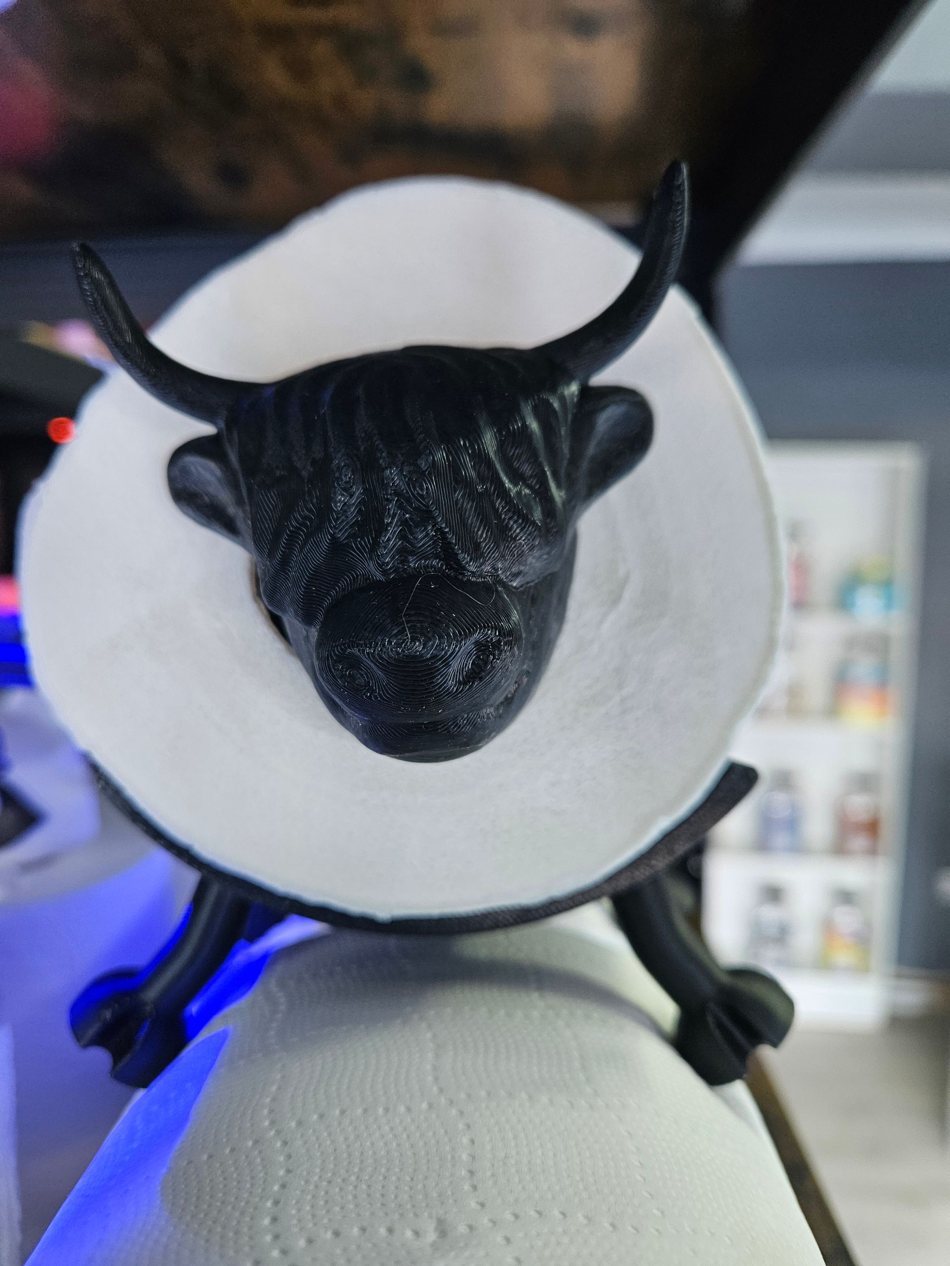Small black horned figurine wearing a white cone collar, lit by a blue glow.
