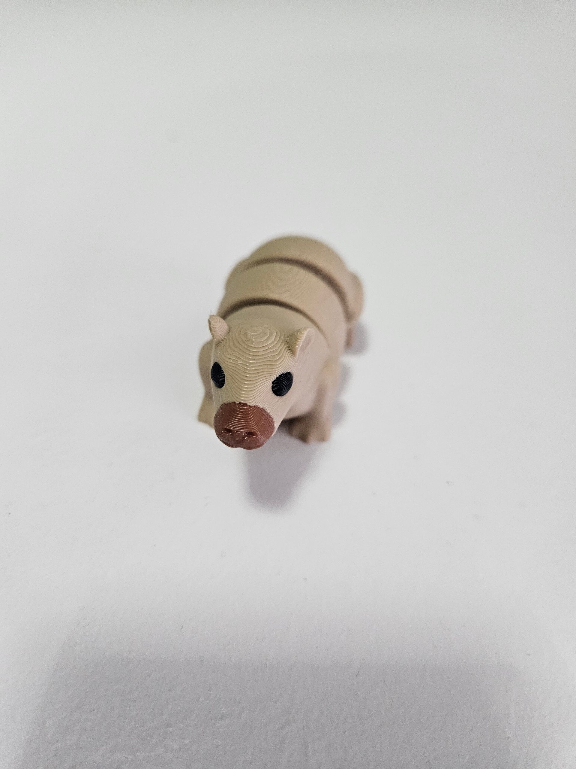 Toy hippopotamus, tan with brown snout and stripes, on white surface.