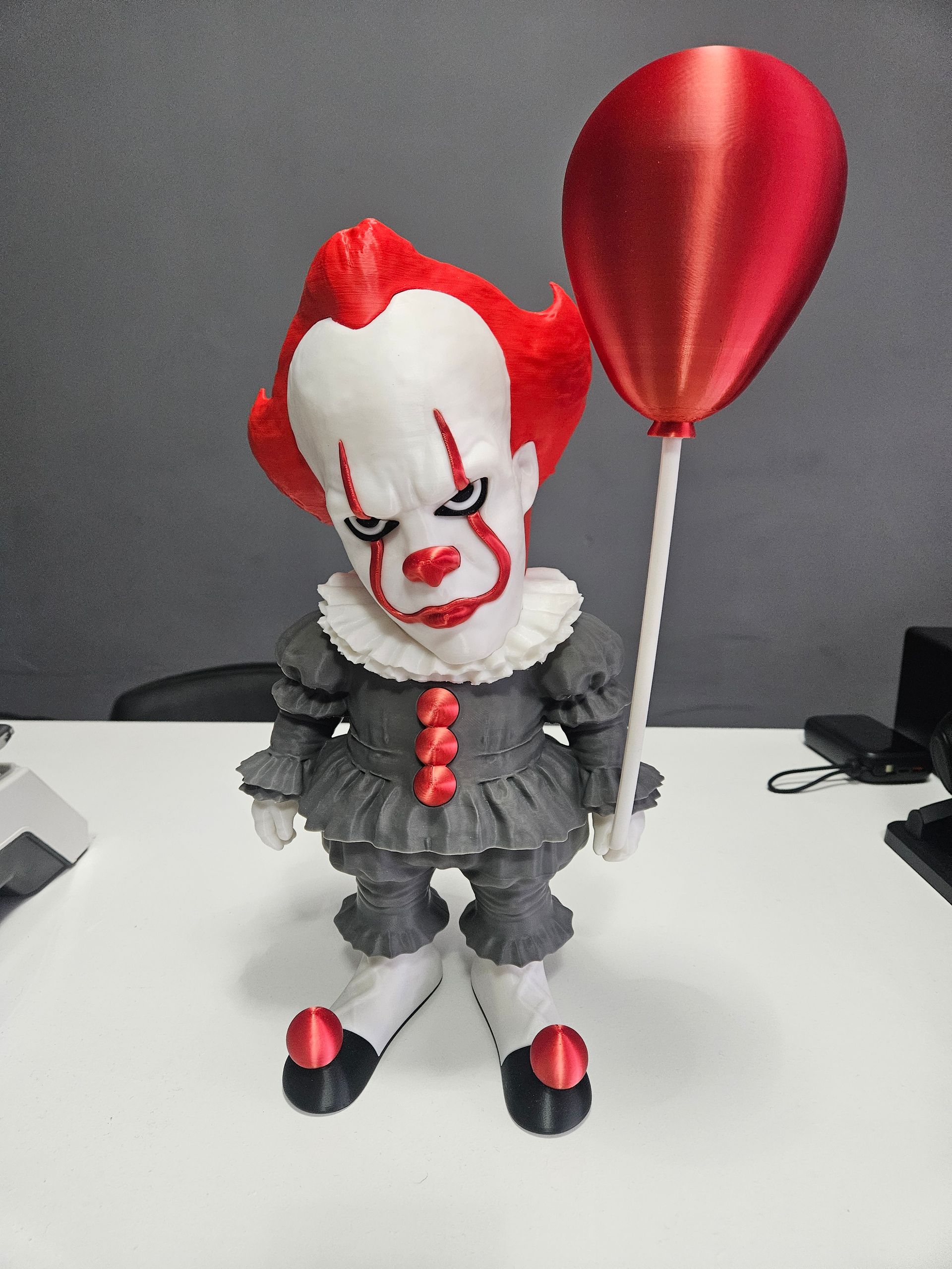 Clown doll holding a red balloon, standing on a white surface against a gray background.