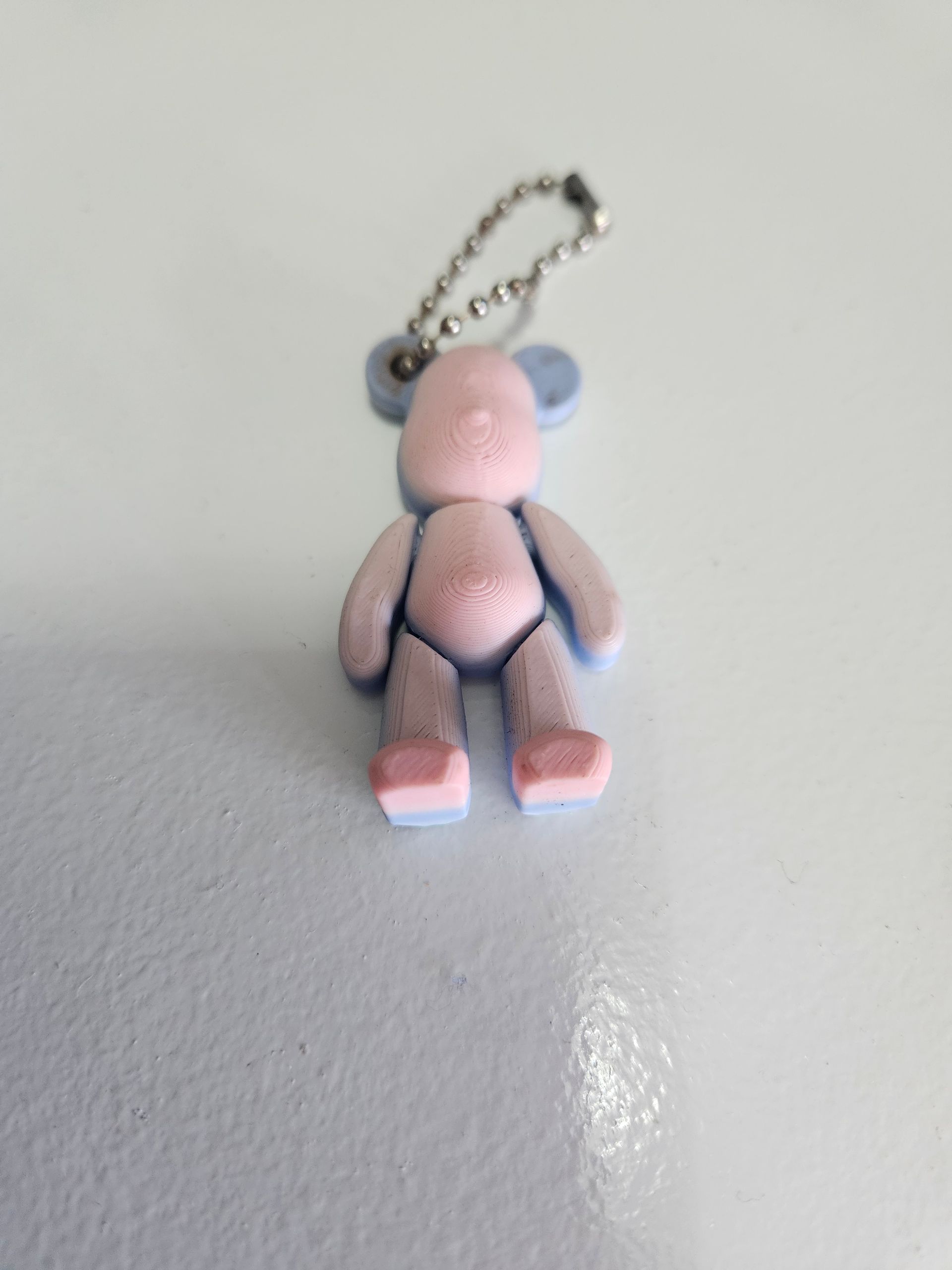 Small pink and gray teddy bear keychain on a white surface