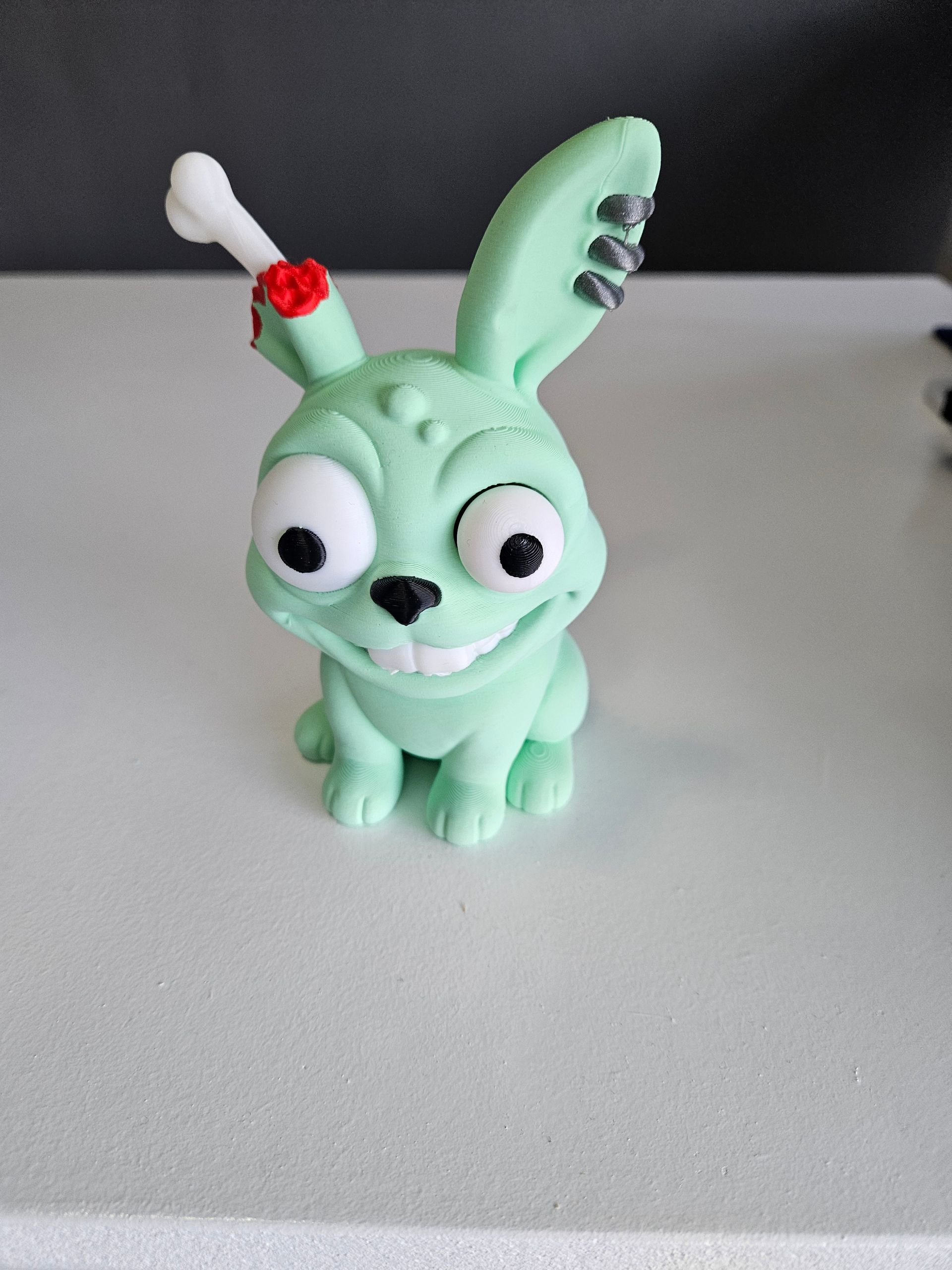 Green zombie bunny figurine with bone sticking out head, sitting, white eyes.