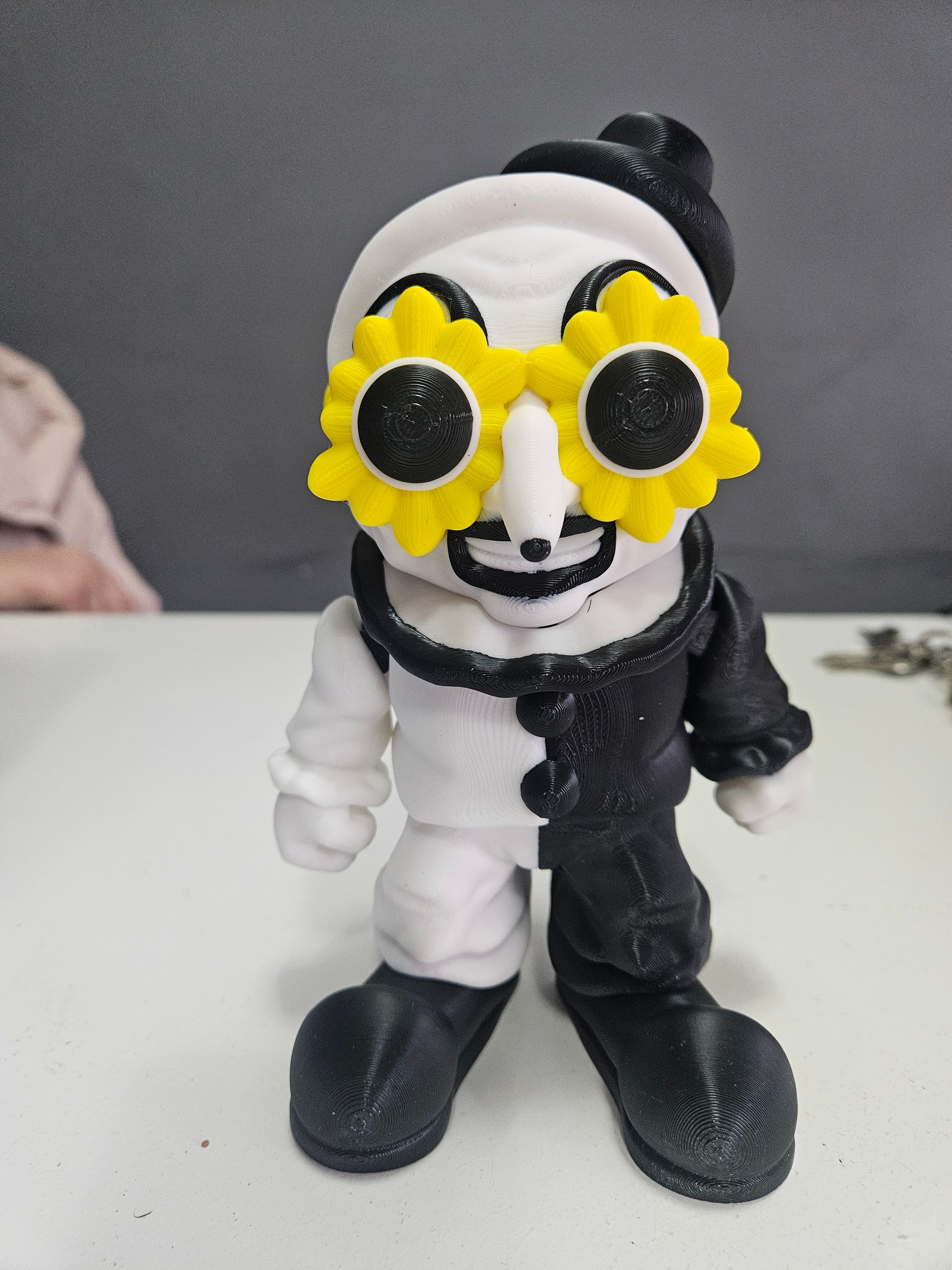 Toy clown figure, half white, half black, with sunflower glasses and a white hat.