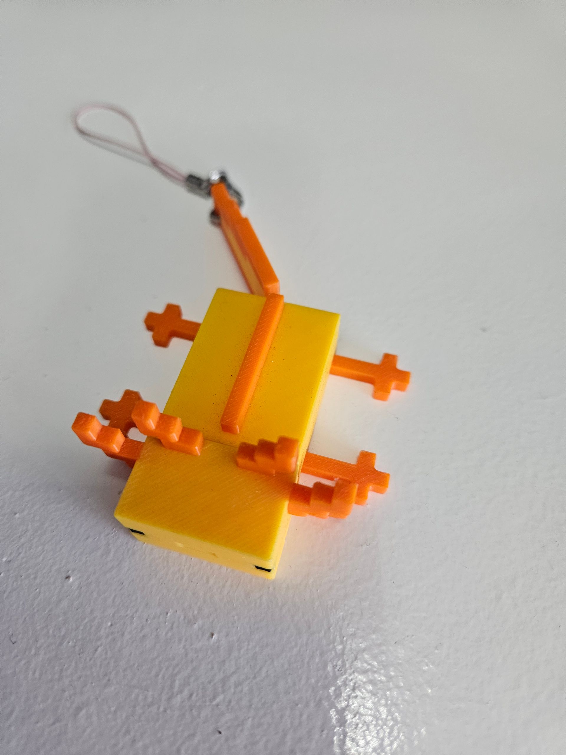 Orange and yellow toy robot with a looped string, lying on a white surface