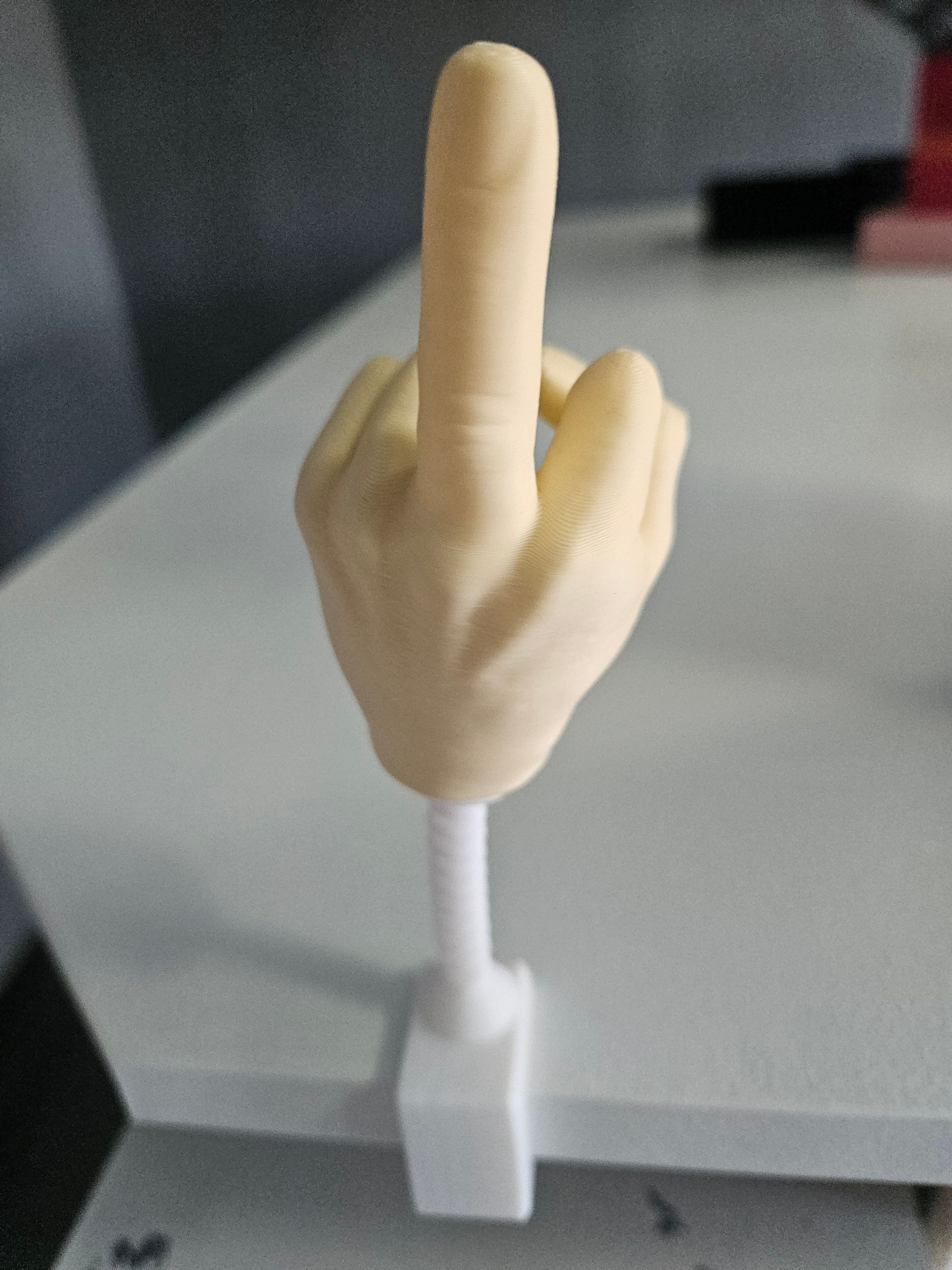 A hand with the middle finger raised, mounted on a white spring and base on a table.