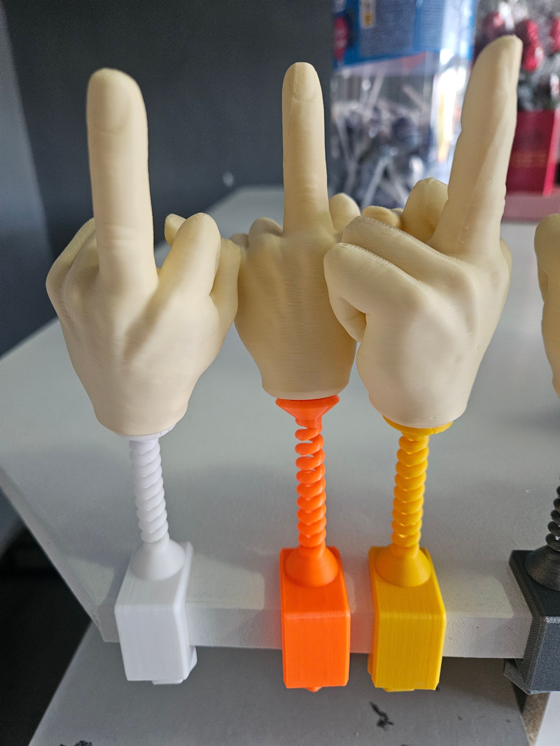 Three novelty hand figurines with raised middle fingers, each on a colored spring base attached to a clamp.